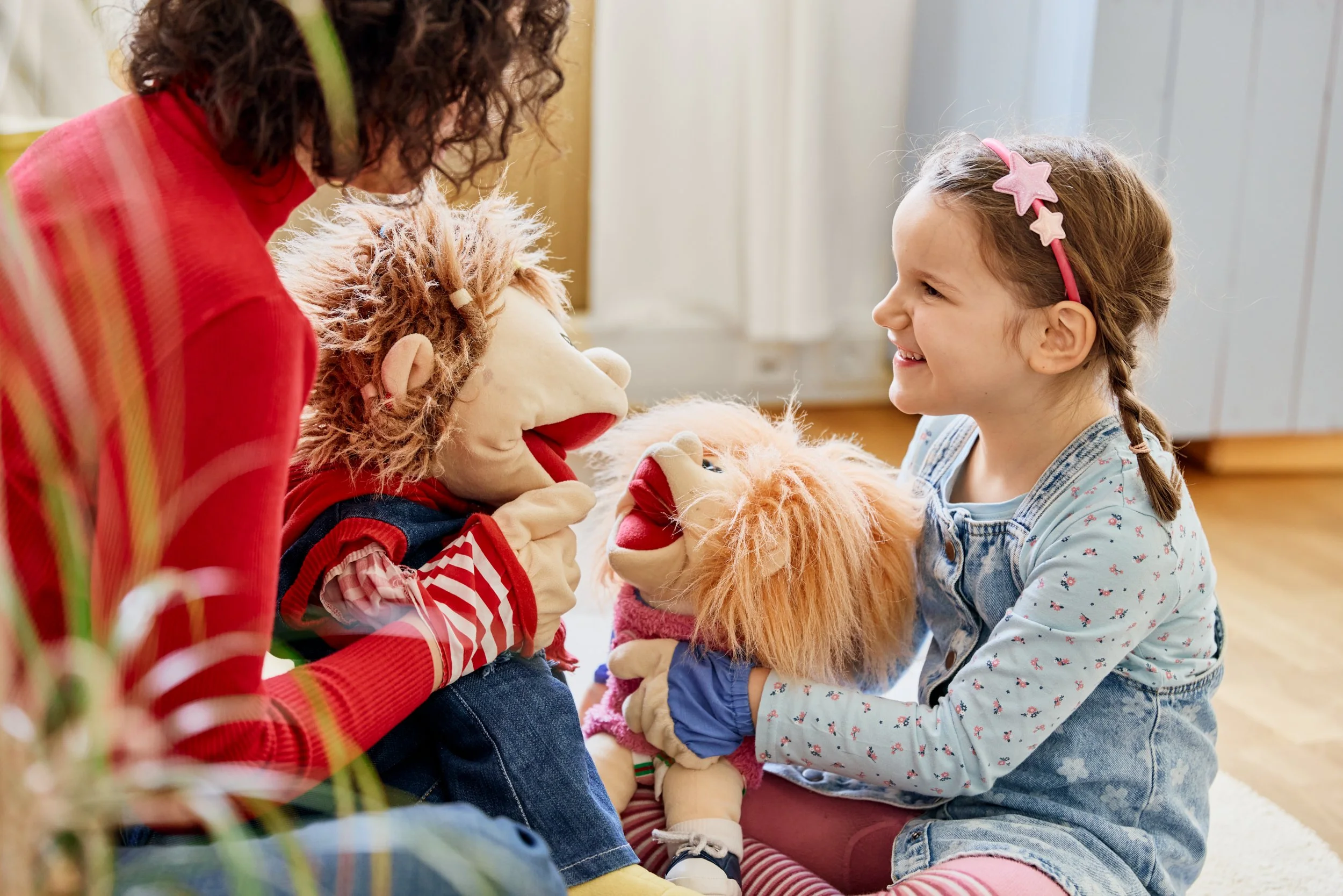 Zwei Mädchen spielen mit Handpuppen in einem Wohnzimmer.