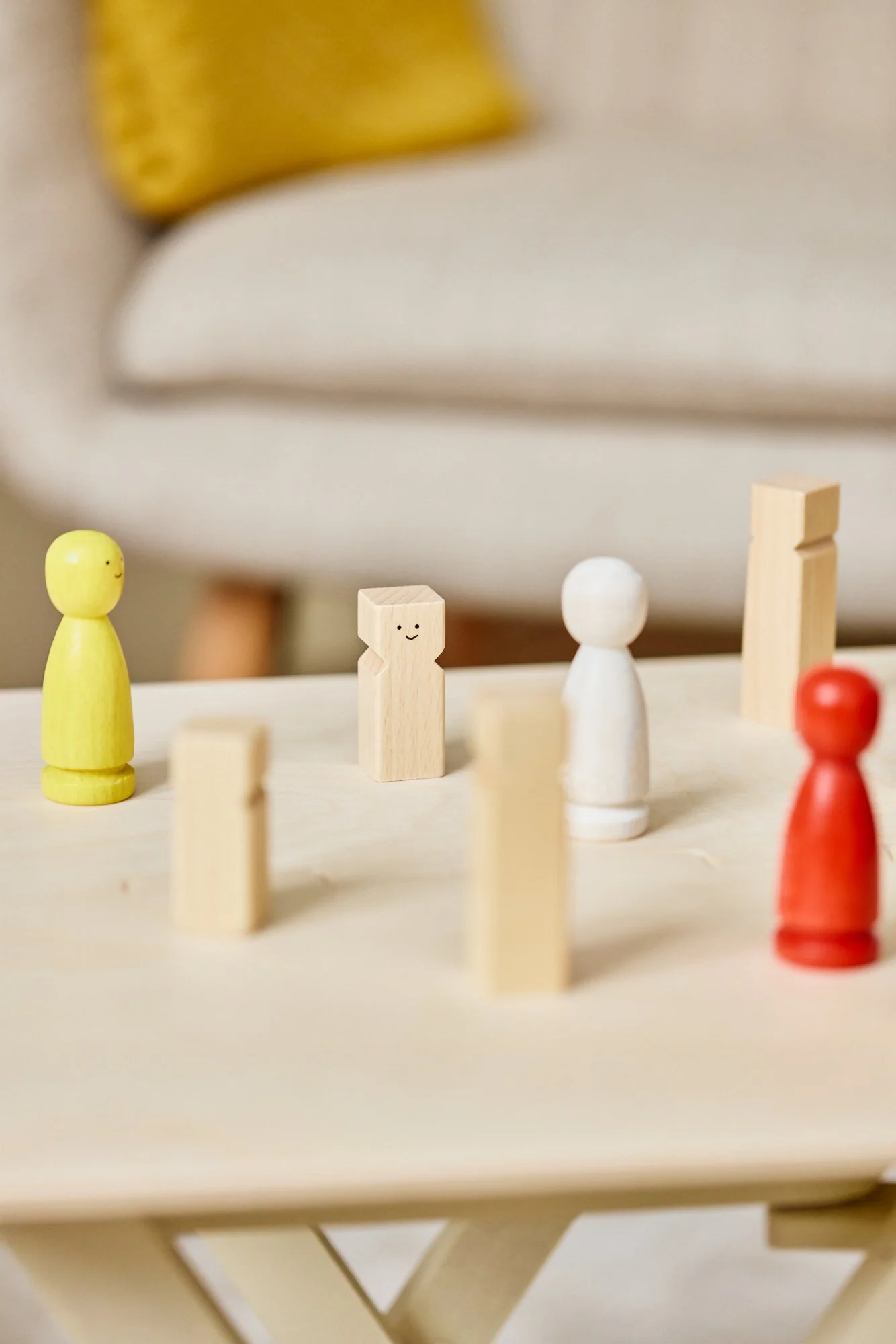 Bunte Spielfiguren auf einem Holztisch, gelb, weiß, naturfarben, rot, mit smiley und minimalistischen Gesichtsausdrücken.