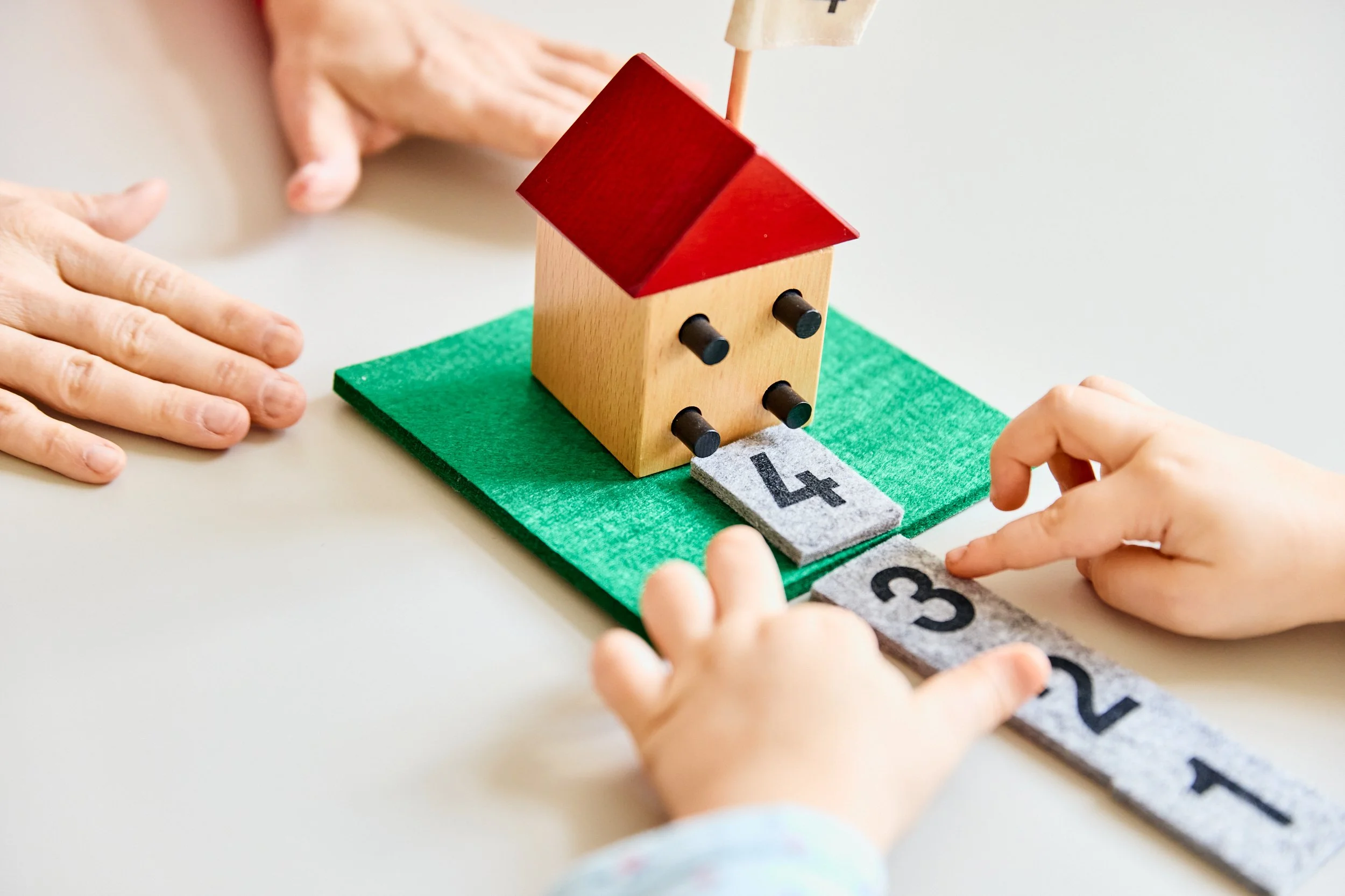 Ein Holzspielhaus mit rotem Dach, das auf einem grünen Filz liegt, wird mit bunten Pfeilen und Felder mit Zahlen gespielt.