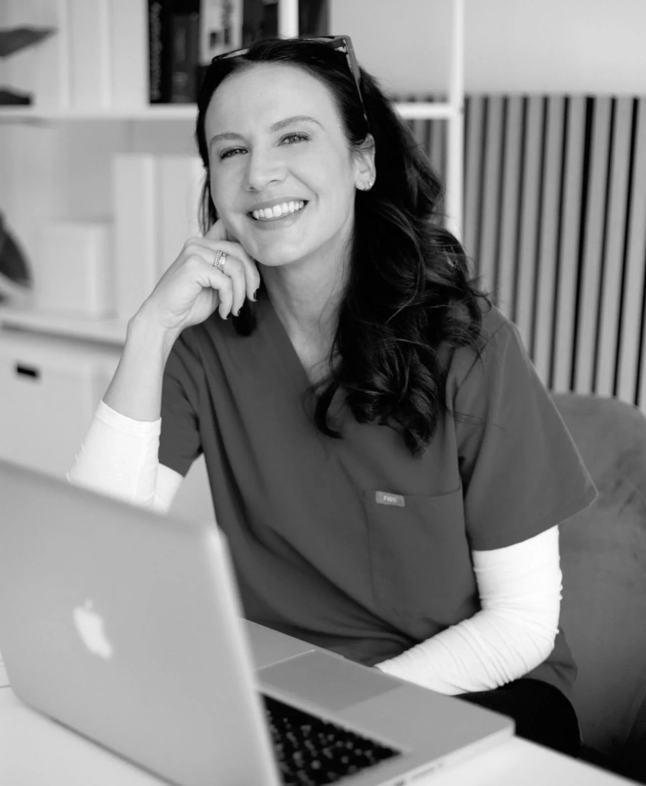 Black and white photo of a Anna Baker smiling and winking, wearing hoop earrings and a star-patterned top.
