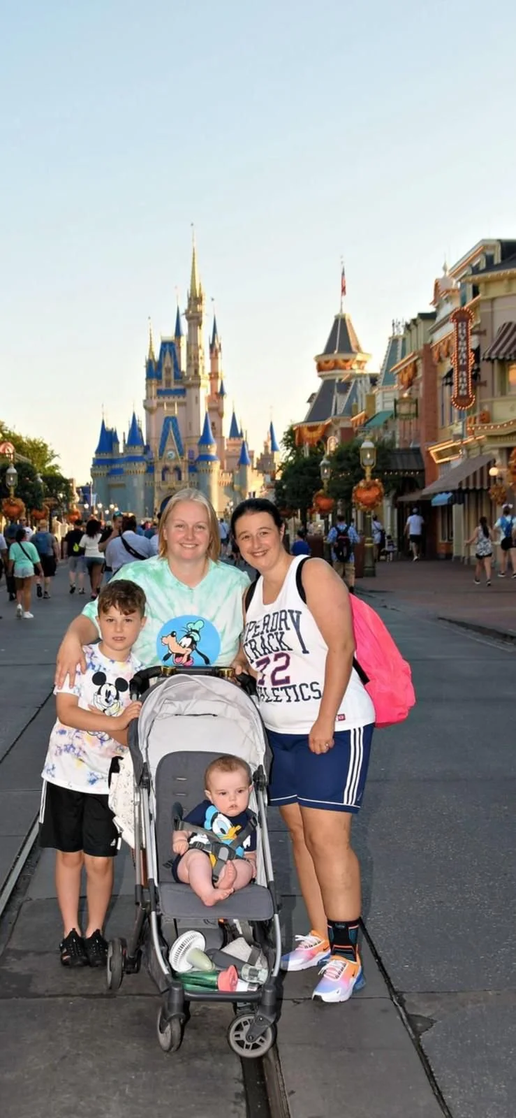 A smiling woman and young boy in a pool, with palm trees and other people in the background.