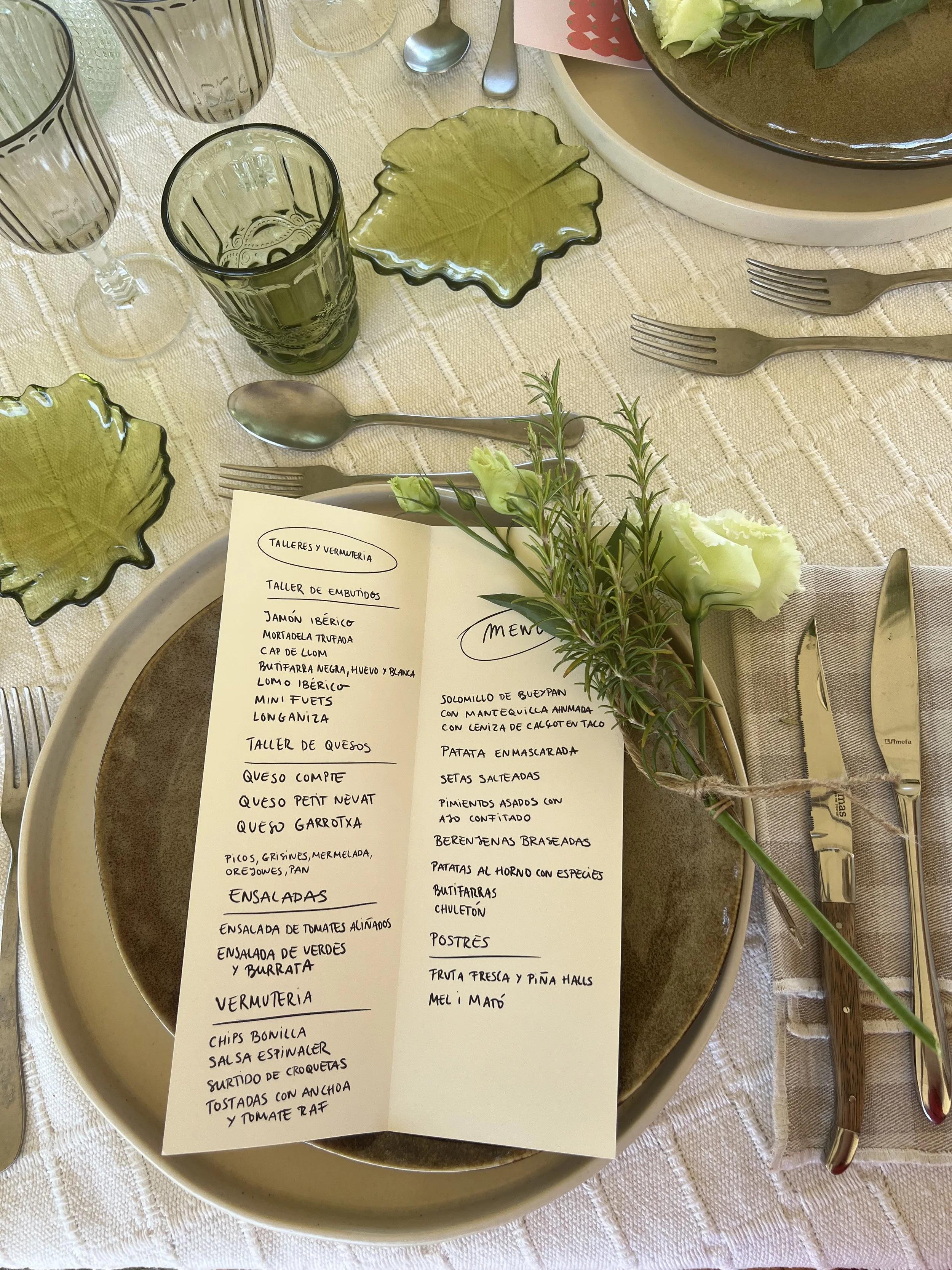 Mesa de comedor con platos, vasos y cubiertos, decorada con flores y una lista de menú en papel.