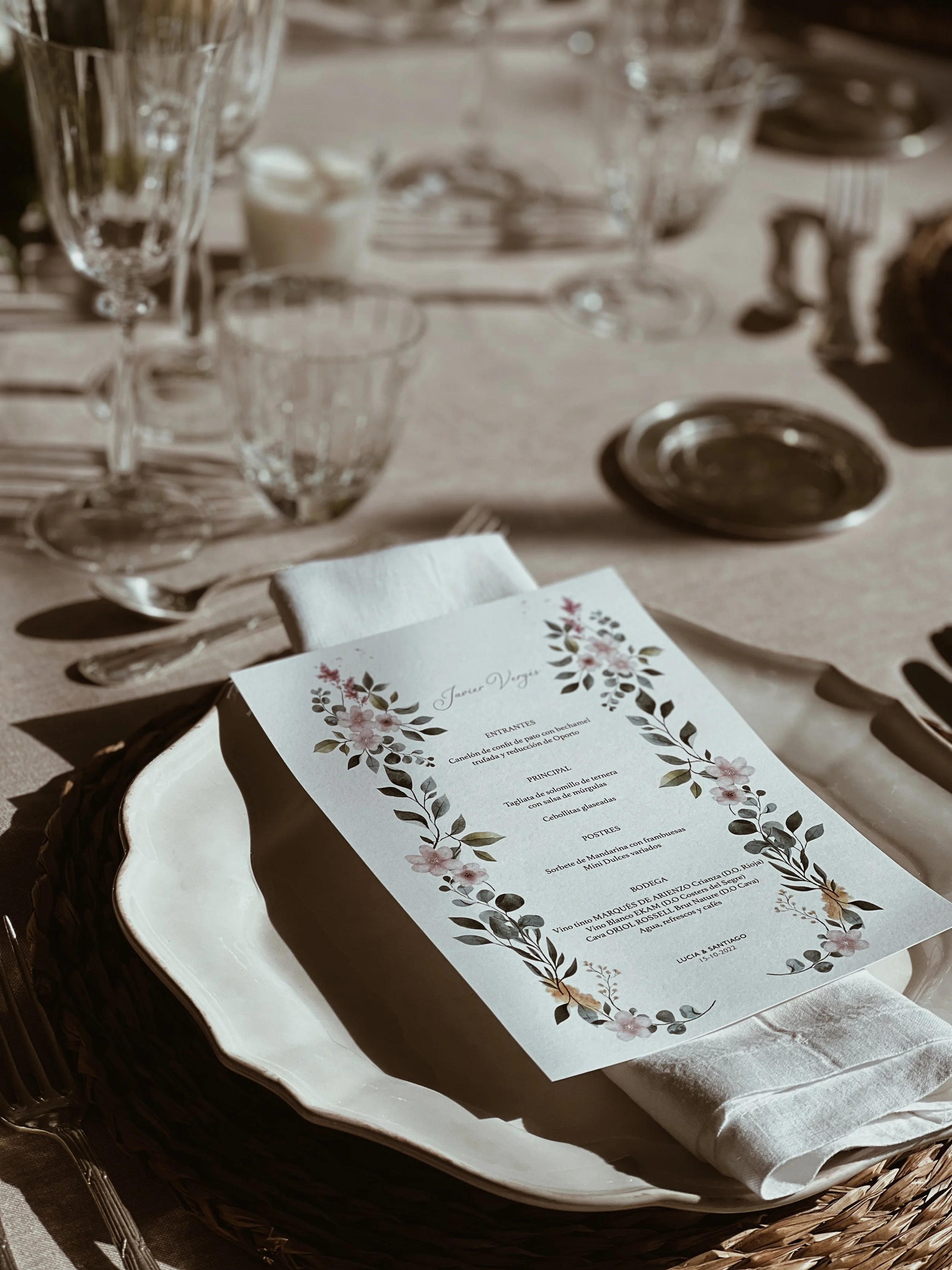 Menú de boda sobre plato, con cristalería y utensilios en mesa decorada con detalles elegantes.