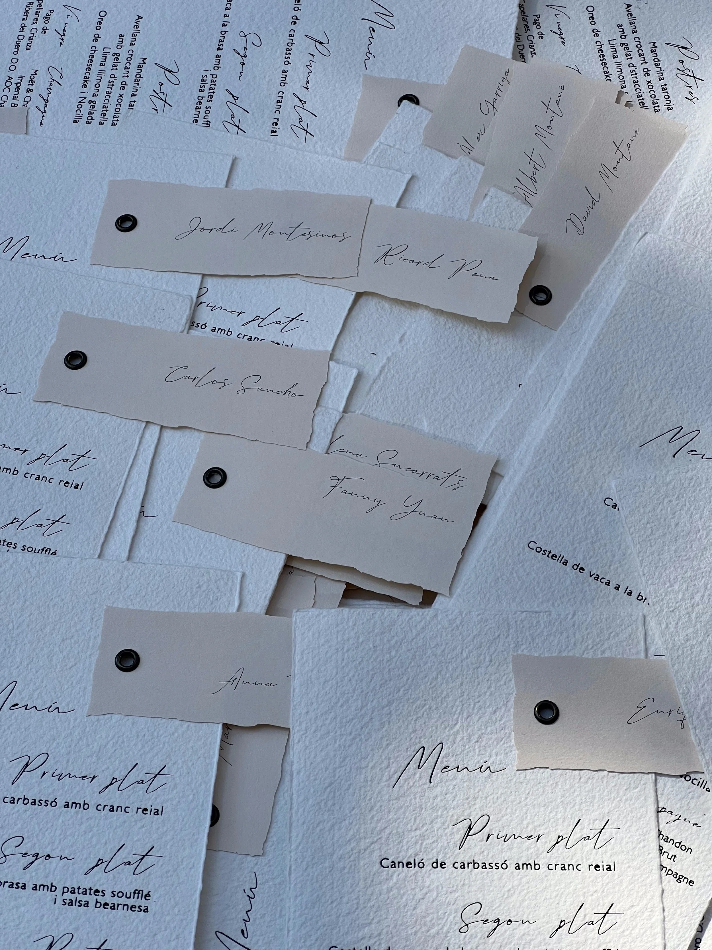 Notas con nombres escritos en cursiva sobre menús impresos y papel rasgado, decorando una pared blanca.