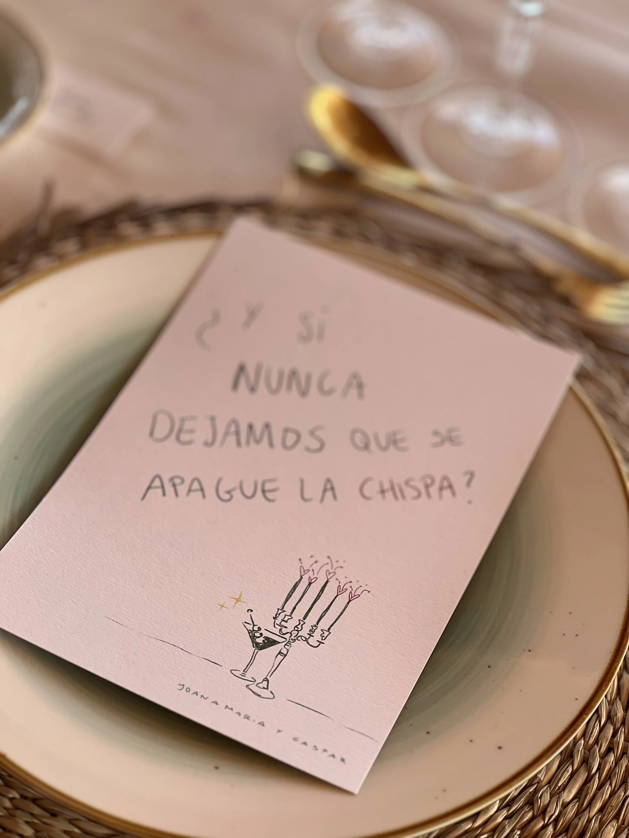 Tarjeta con una cita que dice '¿Y si nunca dejamos que se apague la chispa?' junto a un dibujo de una vela con varias llamas decoradas con corazones, en un plato con cubiertos dorados y alrededor, copas y bebidas en un ambiente elegante.