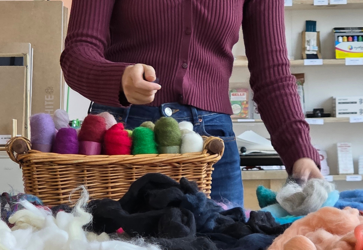 Person browsing at a craft store with colourful felting yarn roving in a basket on a table.