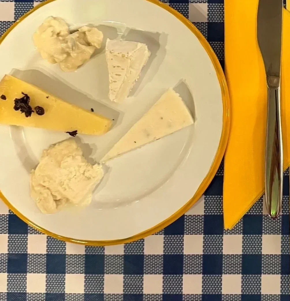 A plate with five different kinds of cheese, a yellow napkin, and a knife on a checkered tablecloth.
