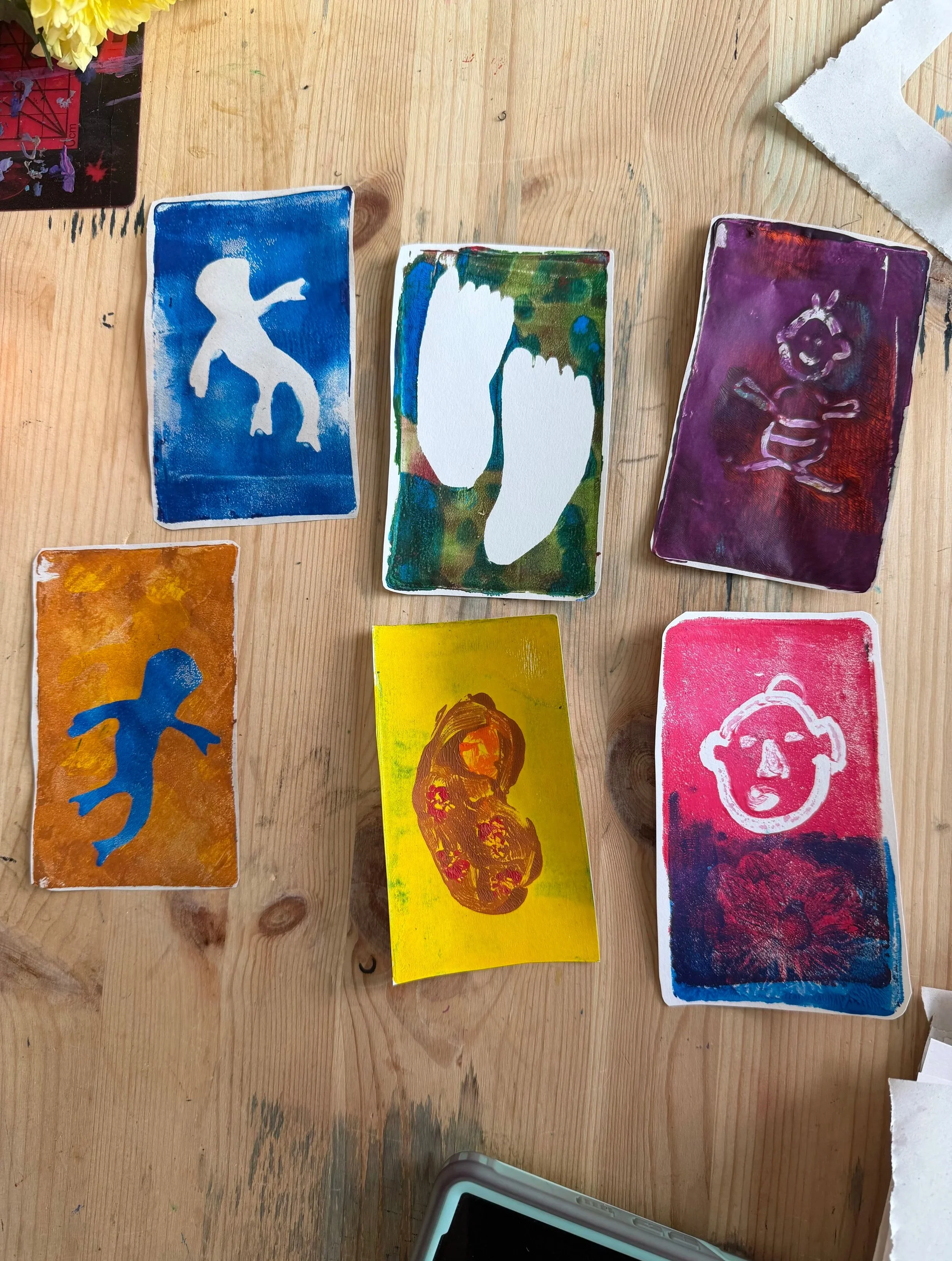 Several colourful gelli prints with colorful abstract designs. One card features a white silhouette of a person, another has a blue figure, another displays a pink skull, and others have various abstract shapes and colors.
