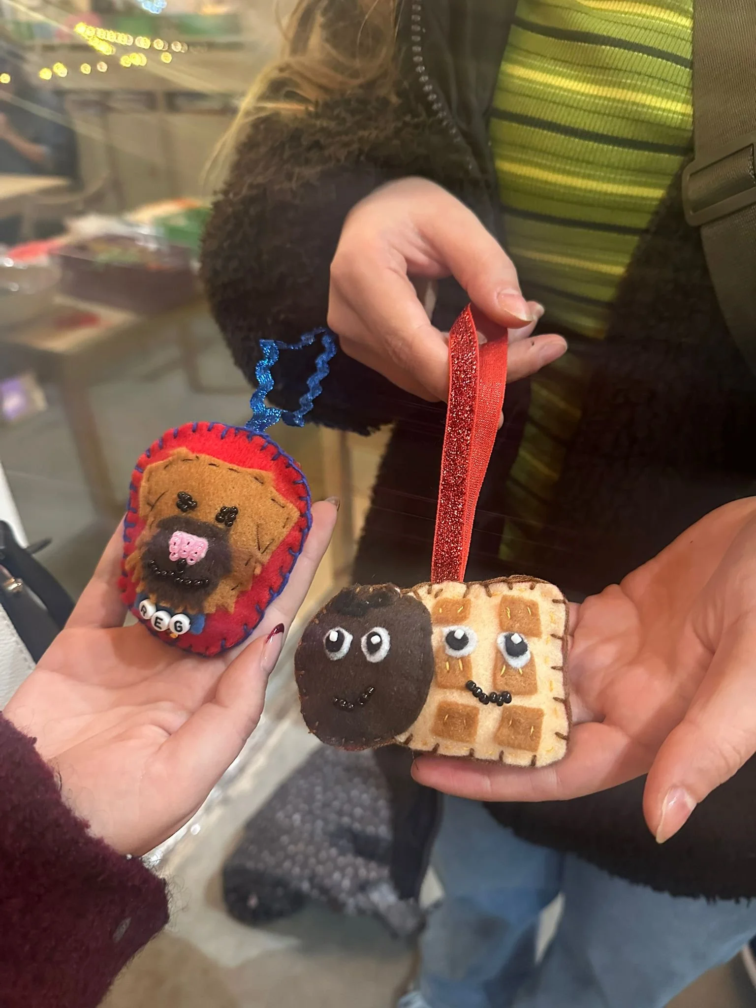 Two people holding up felt ornaments with embroidered animal faces, including a monkey and a bear, at a craft workshop in London.
