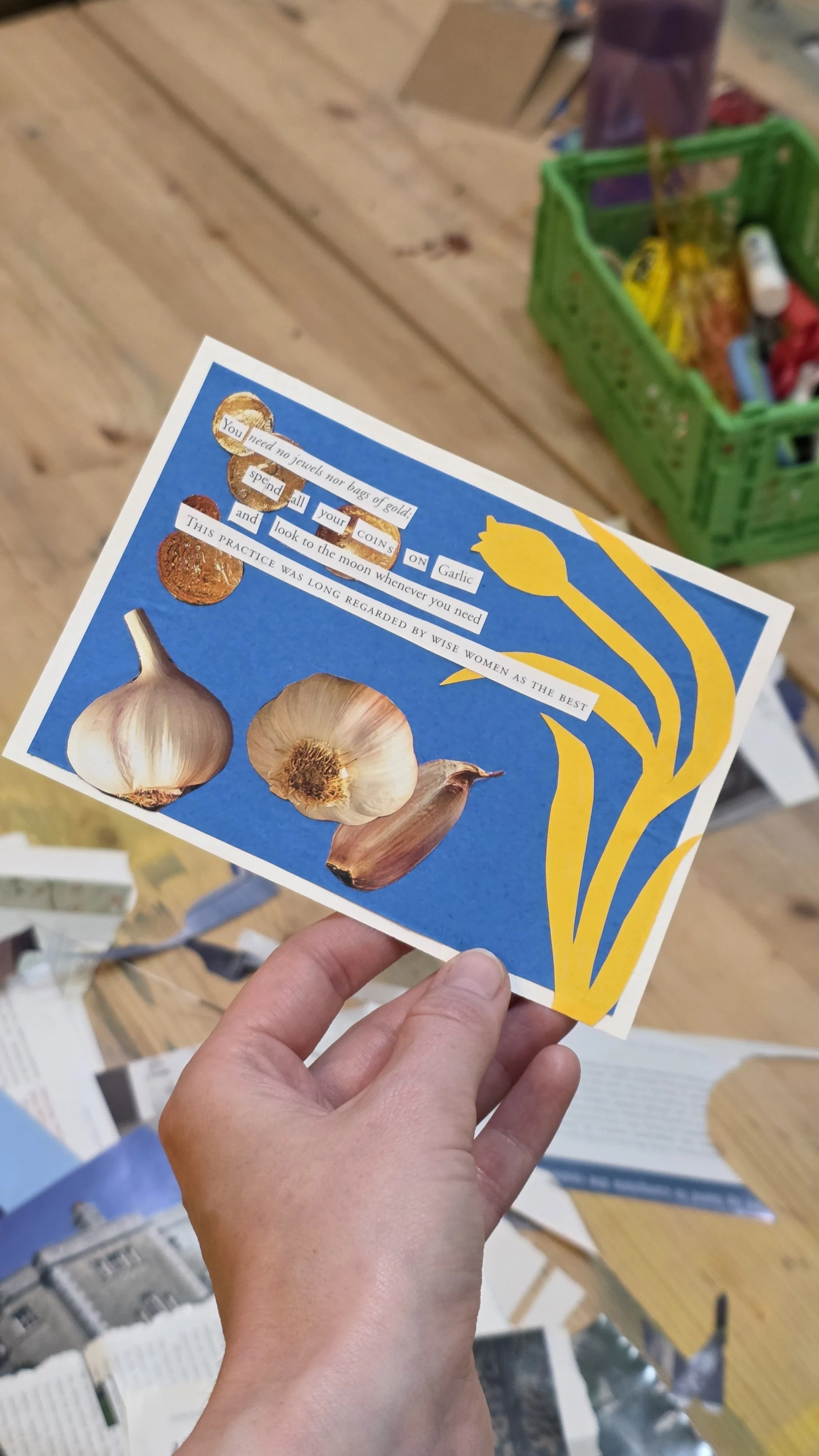A person holding a colorful collage with a blue background, featuring images of garlic and coins, and a yellow scalloped decorative pattern on the right side. The card has a poem or message about garlic and coins.