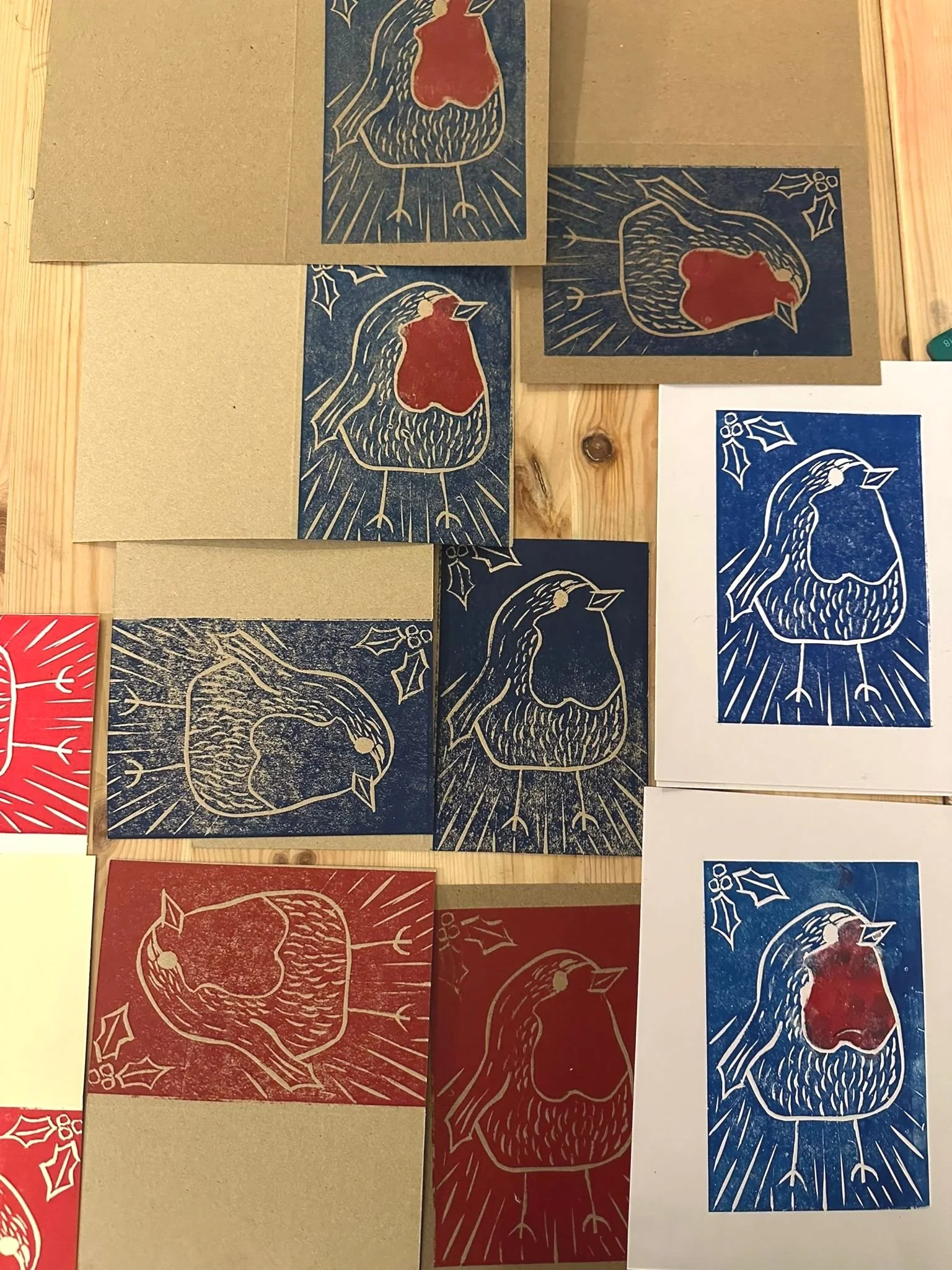 Collection of holiday-themed Linocut prints featuring a rooster with holly leaves, in red, blue, and black colors made at a Lino Print Christmas Card Workshop in London.