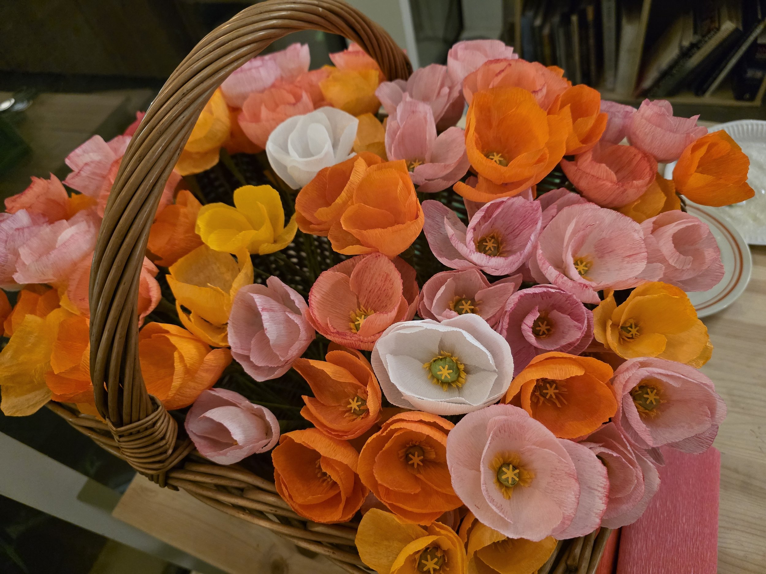 A basket filled with pink, orange, yellow, and white handmade paper flowers.