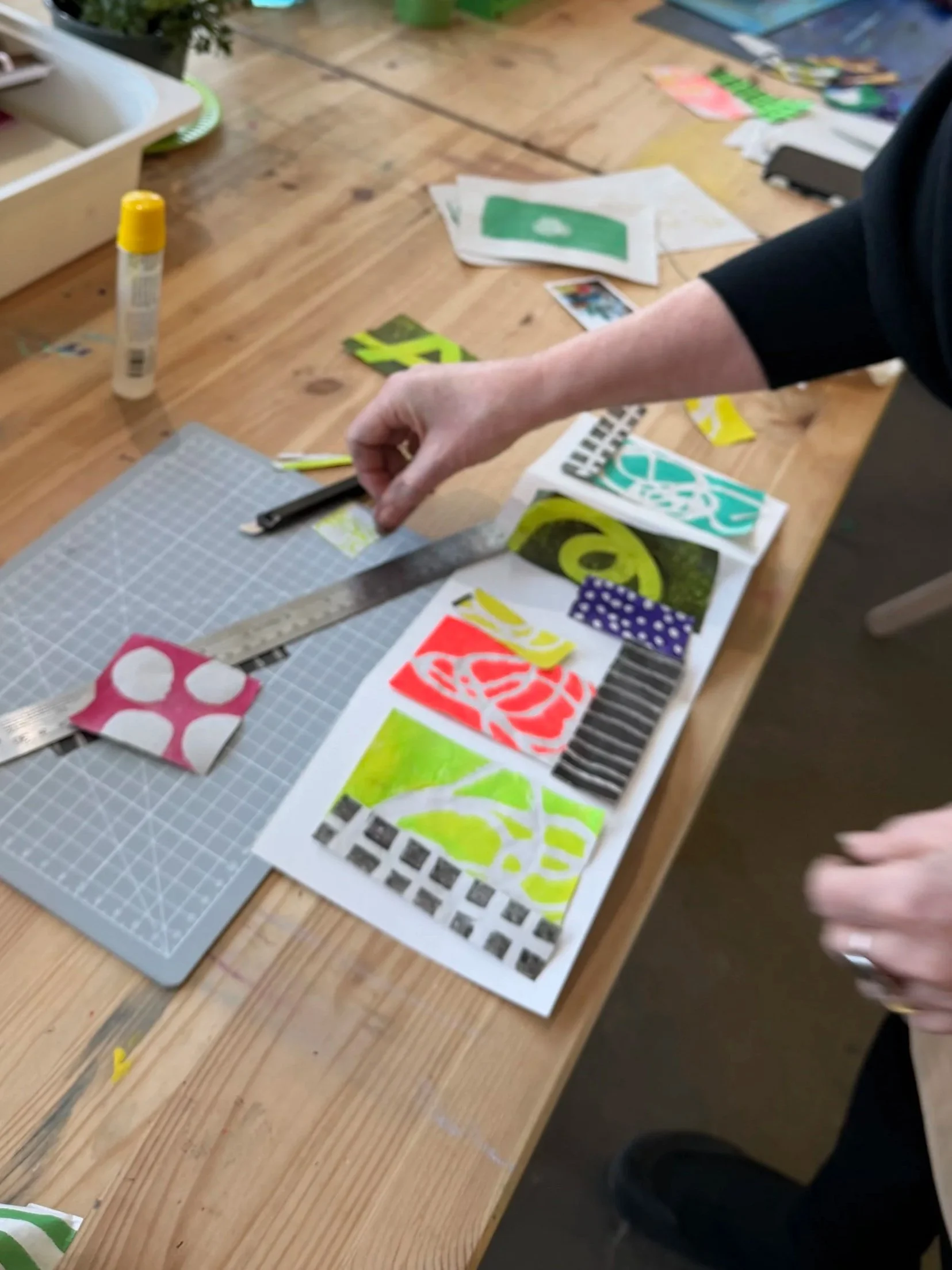 Two women creating floral prints with gelli plates at a table with various craft supplies.