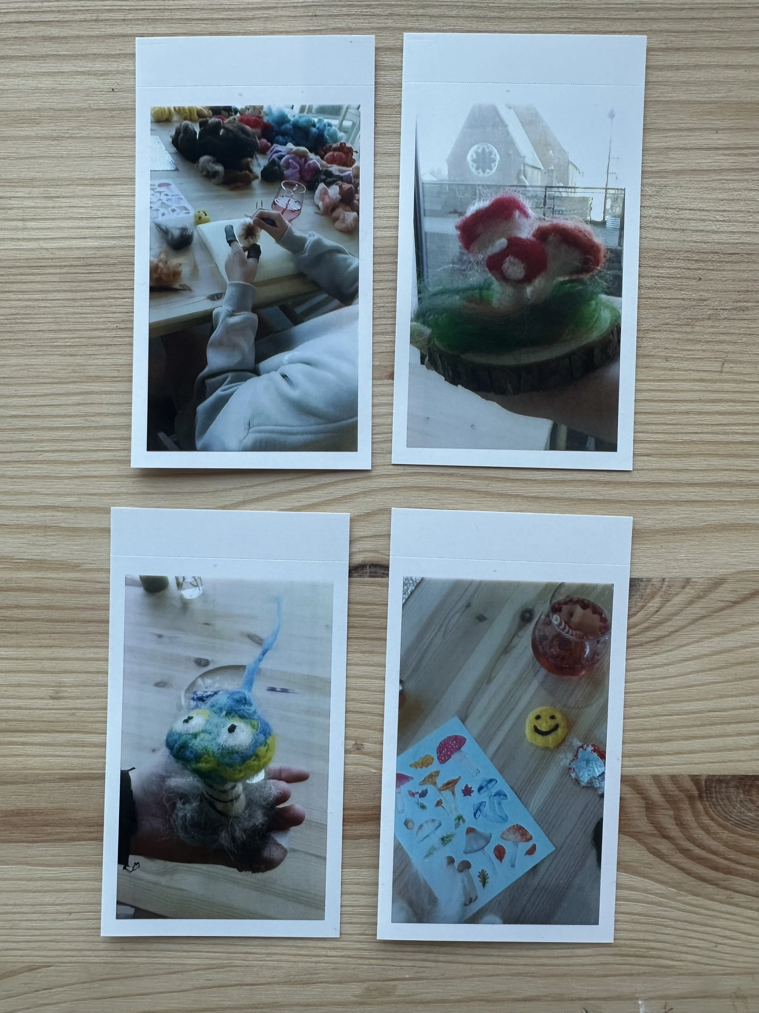 Four printed photos on a wooden surface. The top left photo shows hands working on a craft project with colorful wool and yarn. The top right photo shows a felted animal figure resembling a bear or dog, held in a person's hand with a building and rooftop in the background. The bottom left photo shows a felted object in a person's hand, with a colorful wool sphere and crafting materials in the background. The bottom right photo shows a workspace with felted animals, a sheet of paper with cut-out shapes, and some completed felted items.