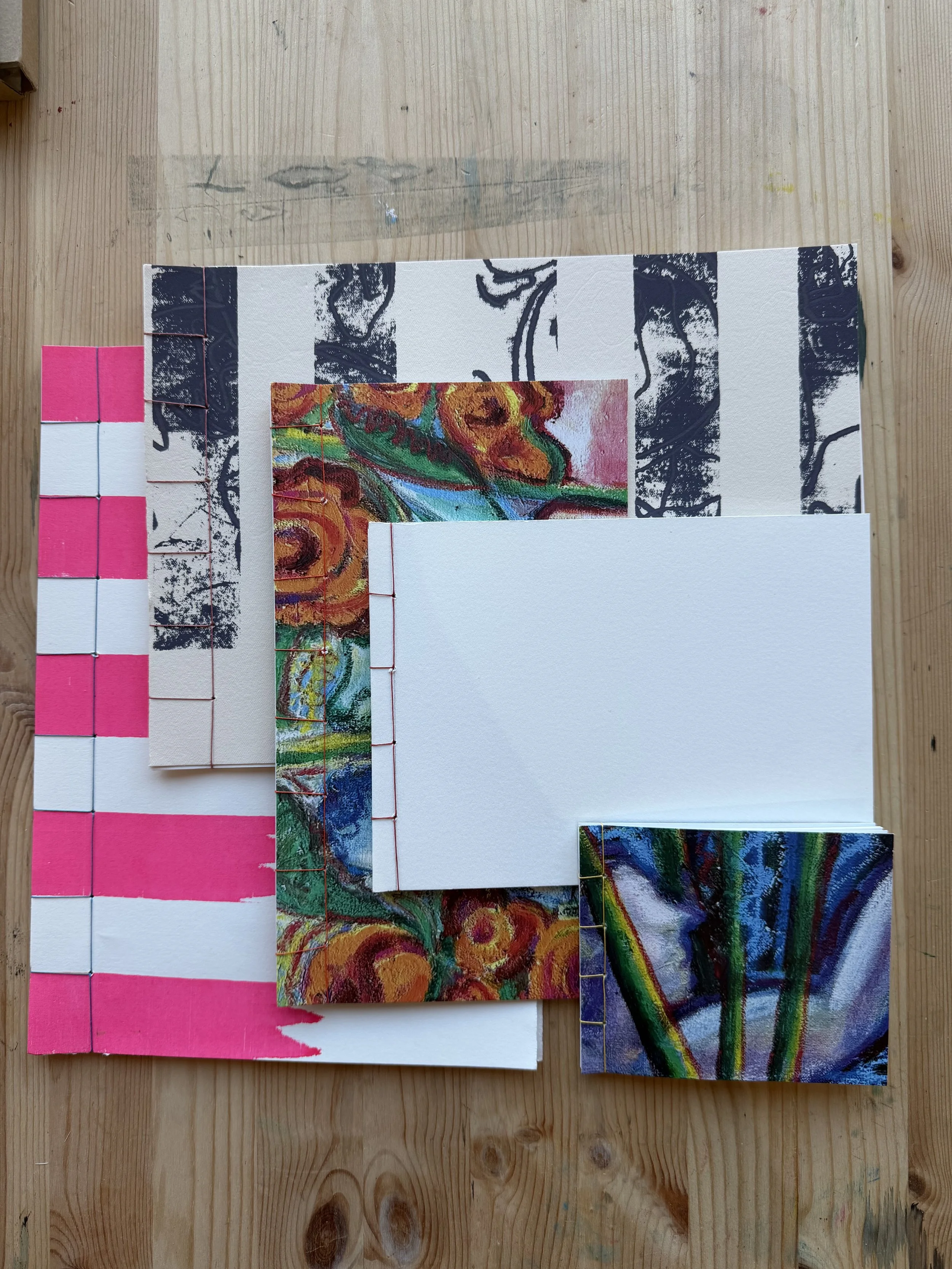 A collection of small paintings, color swatches, and pieces of paper with art and color samples on a wooden table.