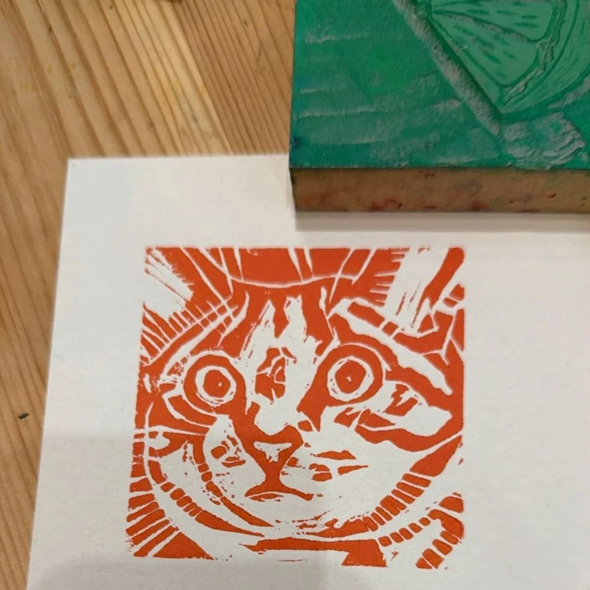 Orange print of a cat's face on white paper with a green block partially visible at the top right corner.