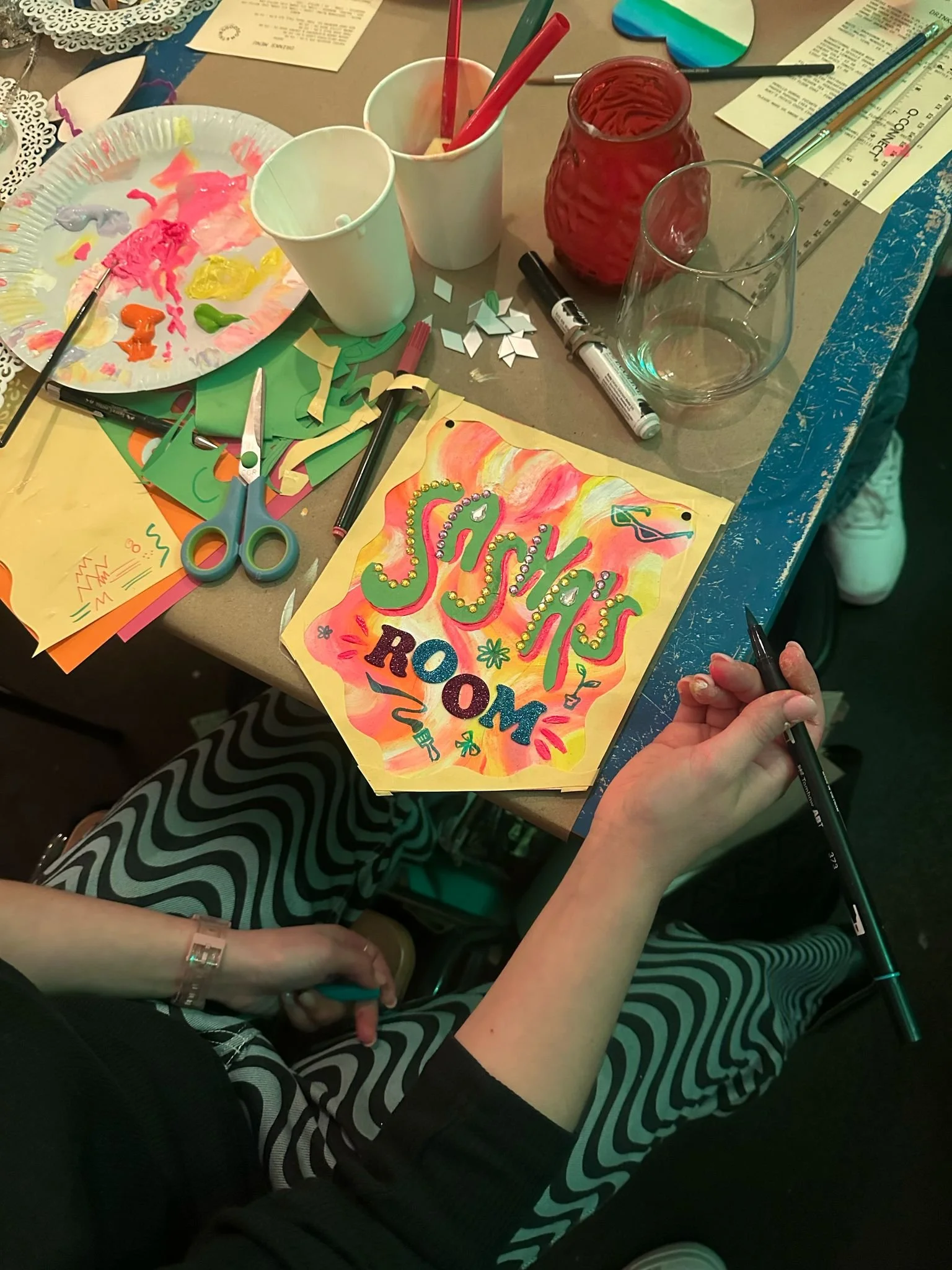 Crafting table with paint supplies, scissors, paper, and a colorful 'Sparkle' card.