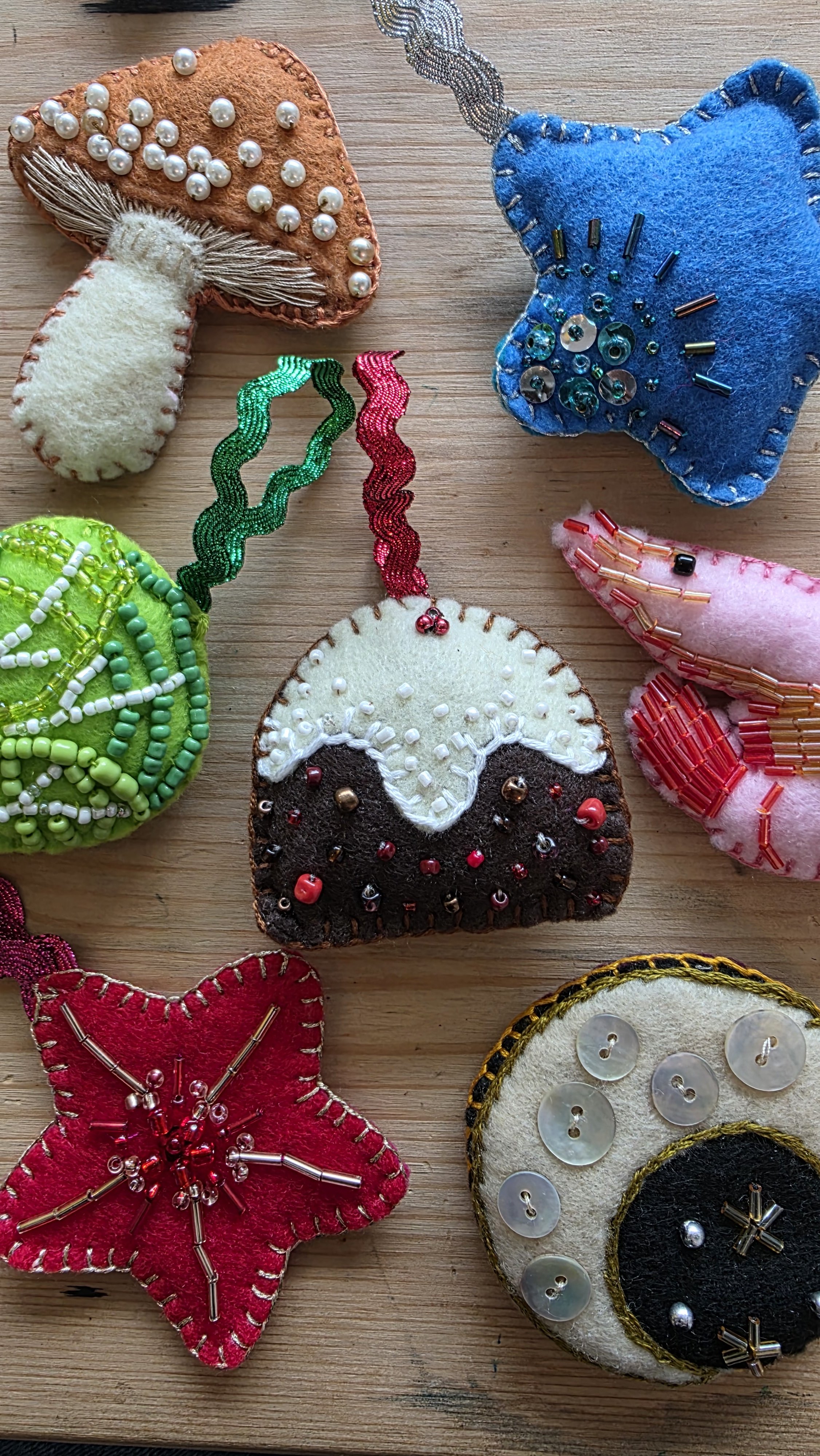 Assorted colorful handmade felt ornaments decorated with beads, sequins, and embroidery, including mushrooms, hearts, stars, and other whimsical shapes.