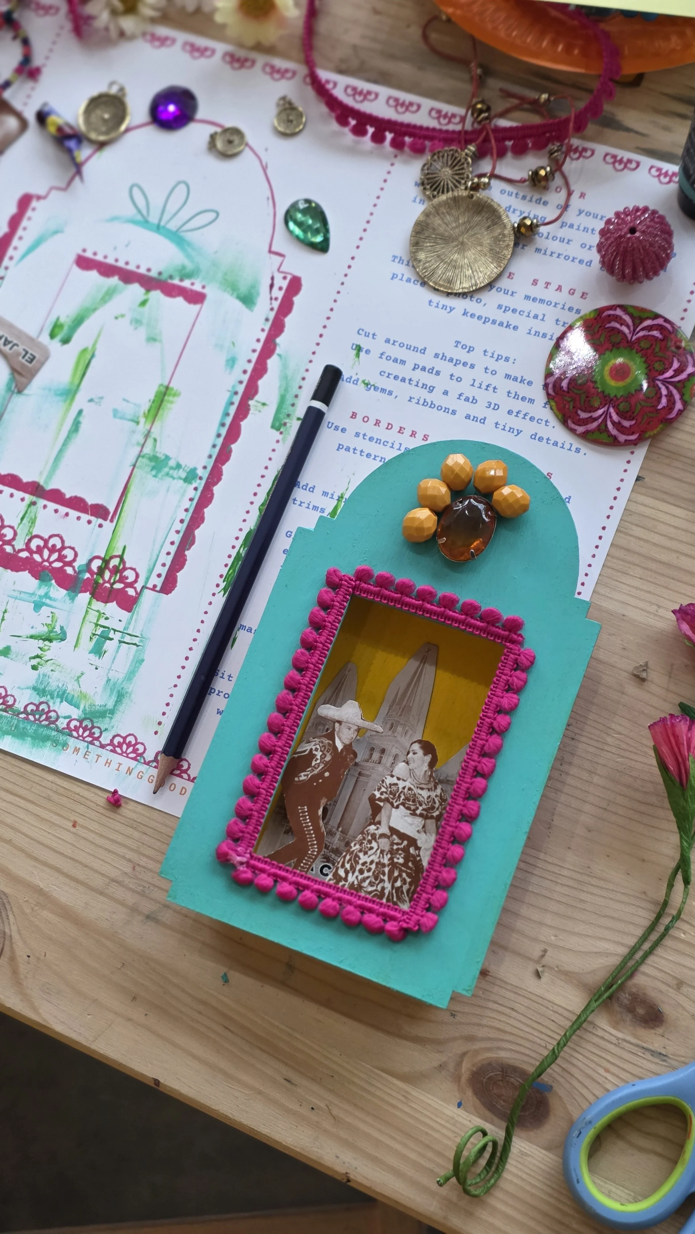 Colorful craft supplies and materials on a wooden table, including photographs, paper, beads, and decorative items for a creative project at a craft workshop.