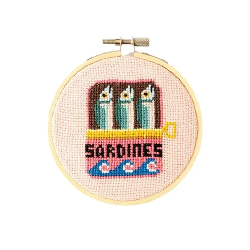 Cotton Clara Cross-stitch embroidery of three sardines, above the word "SARDINES" and blue waves on a pink background, in a hoop.