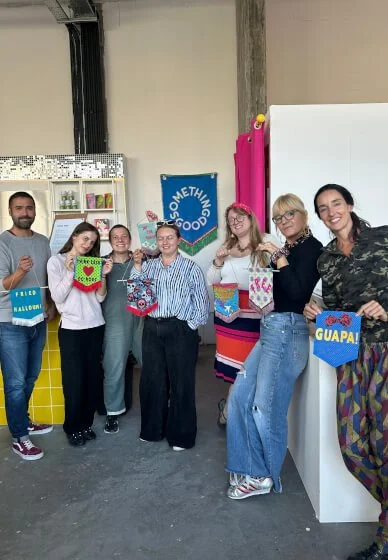 Group of seven people standing together indoors during a celebration, holding colorful handmade fabric signs with cheerful expressions.