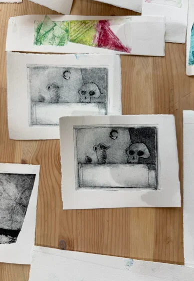 Two tetrapak prints of a dog, a skull, and a ball inside a box, with one print in black and white and the other shaded in darker tones.