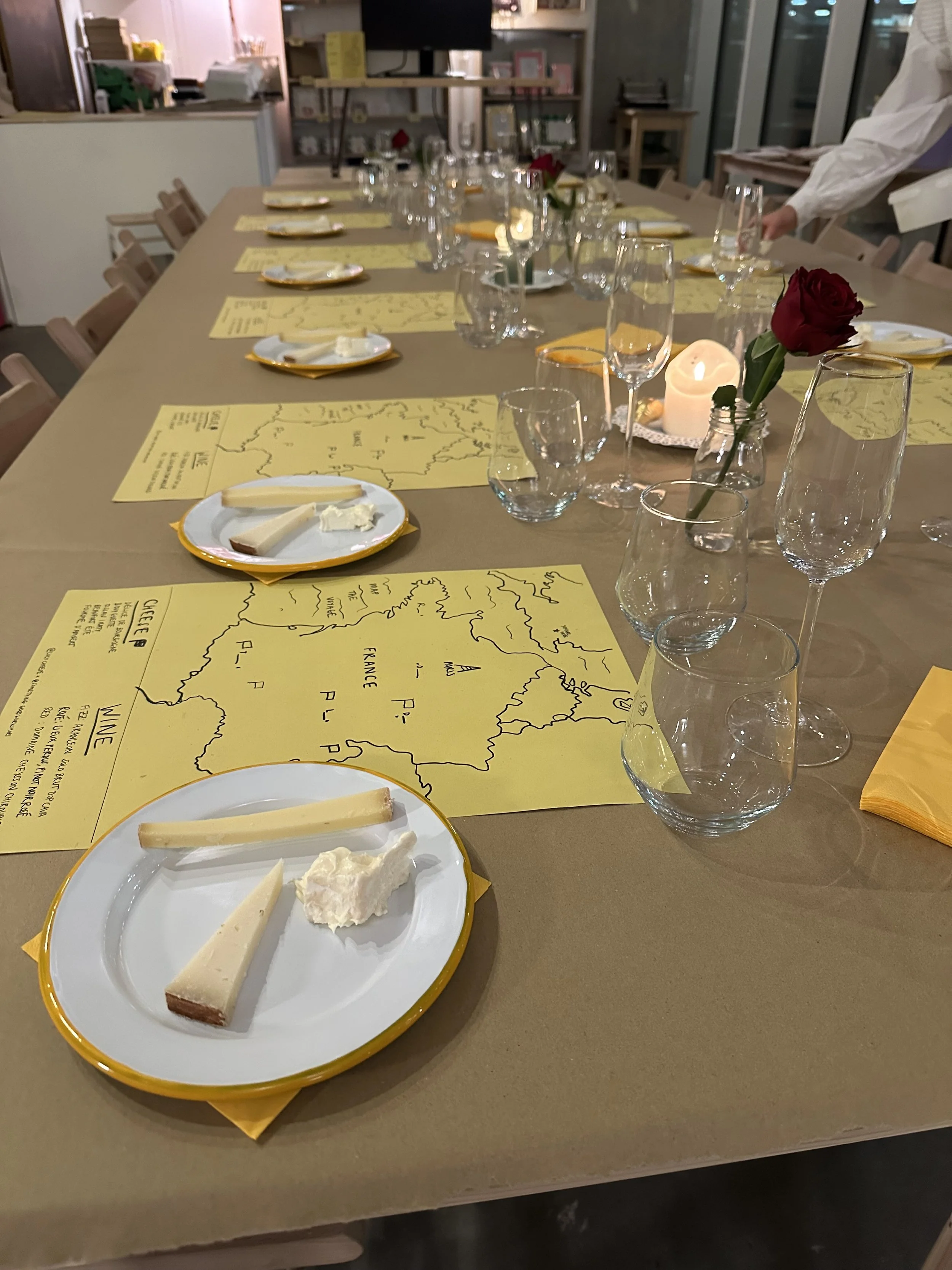 A dining table set with plates of cheese, wine glasses, and centerpieces, in a warmly lit room.