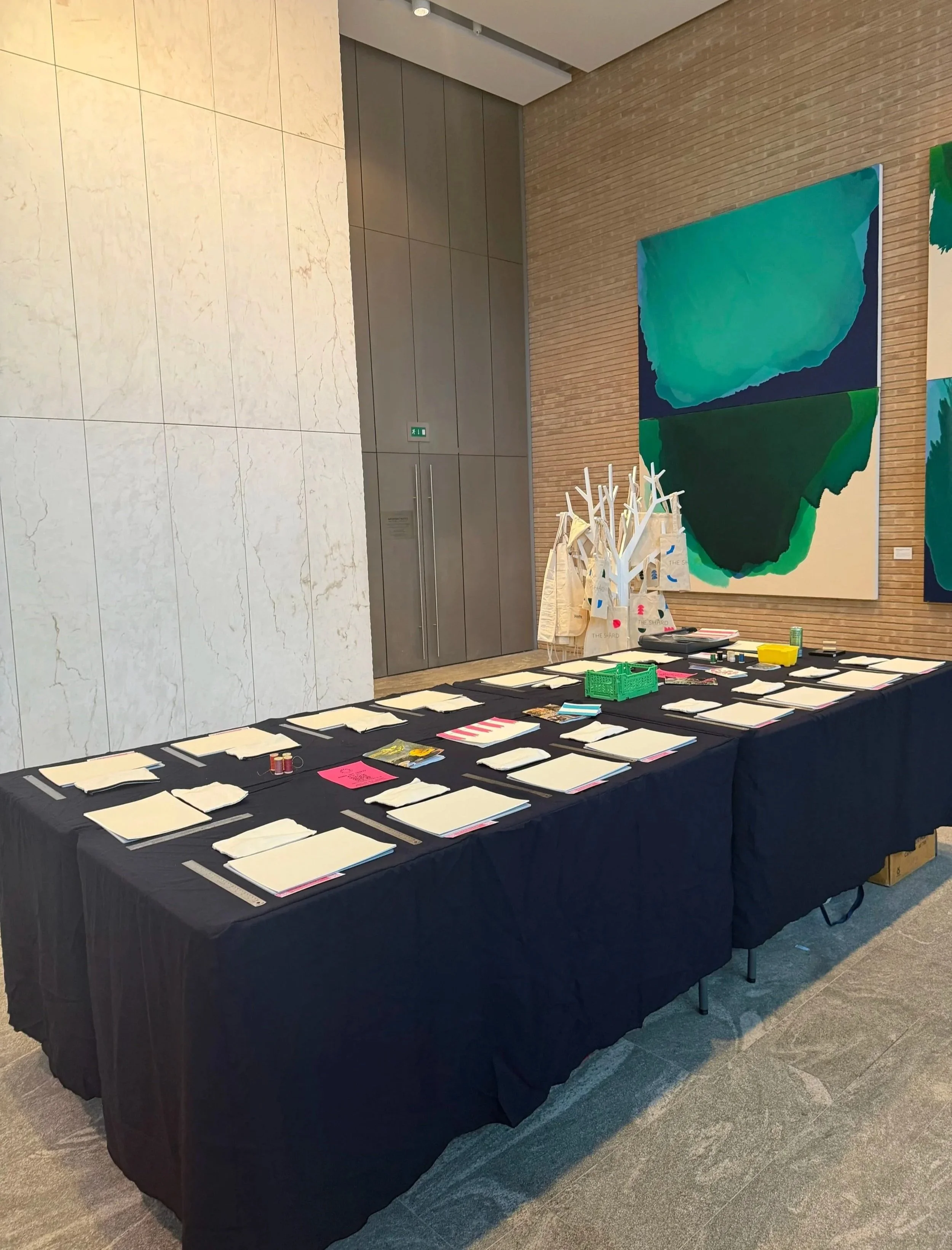 A table covered with a black tablecloth displays stationery and paper items, set in a modern interior with artwork on the wall.
