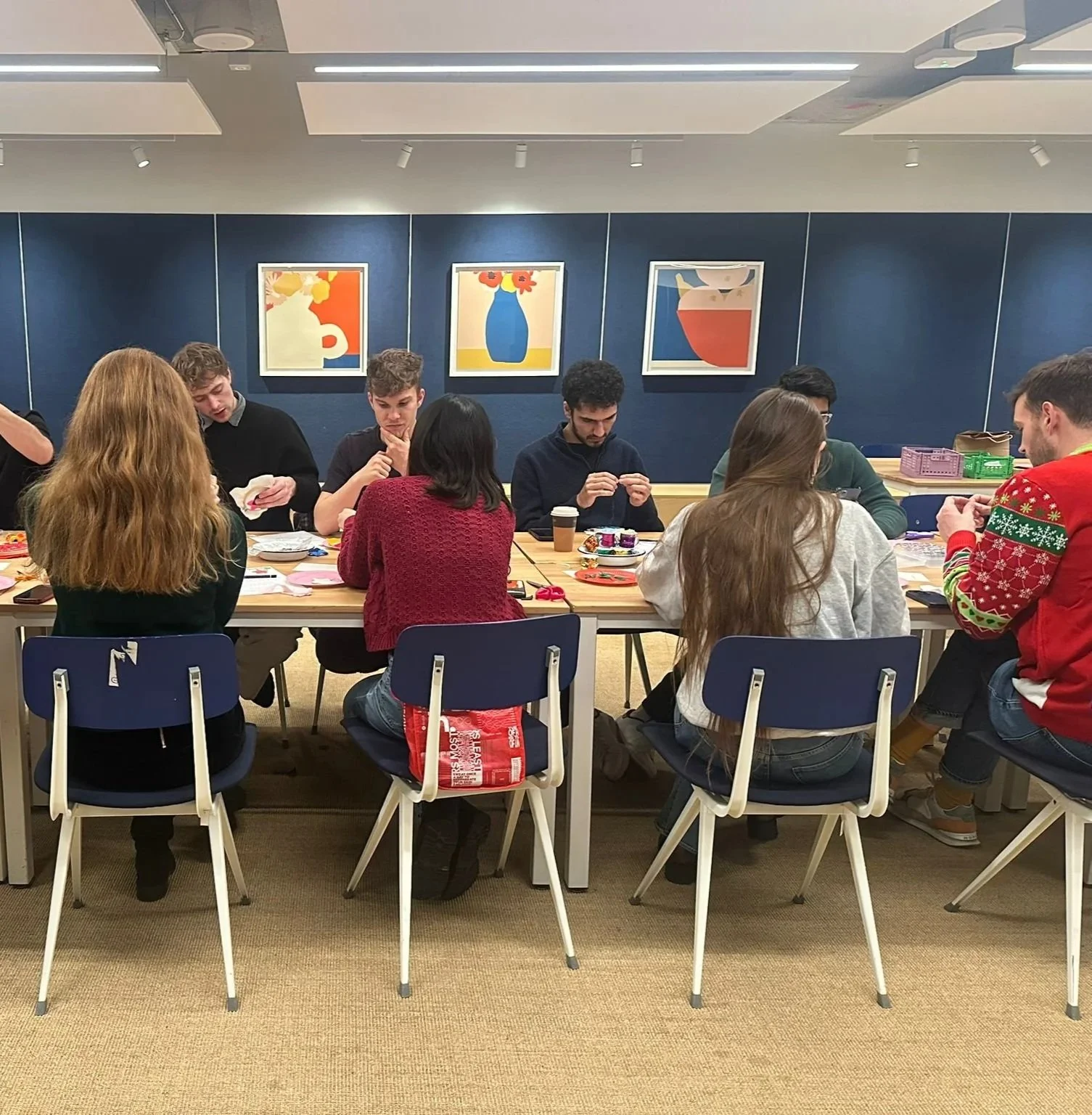 People seated at a table making crafts in a room with blue walls and colorful abstract artwork.