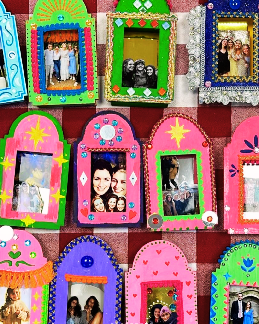 Colorful shrine photo frames decorated with beads, glitter, and emojis, holding pictures of people at a festive gathering, arranged on a checkered red and white cloth.