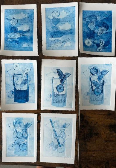 A collage of nine blue print images depicting various objects, including fish, a bottle, a butterfly, and a pencil, arranged on a wooden surface.