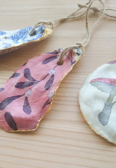Three handmade decoupage christmas ornaments with mistletoe designs on a wooden surface.