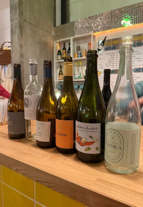 Several bottles of wine and a glass bottle with a light-colored liquid on a wooden bar counter.