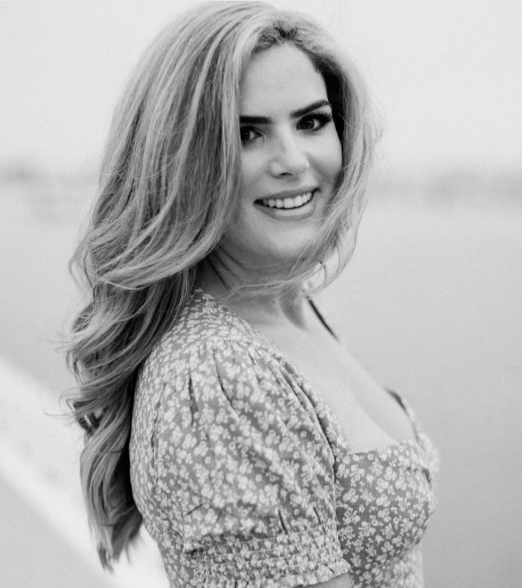 Black and white portrait of a smiling woman with long wavy hair wearing a floral dress.