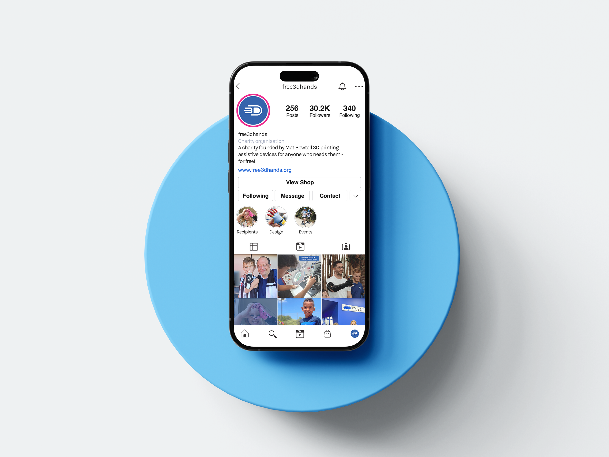 Smartphone displaying an Instagram profile for free3dhands, a charity organization, on a blue circular surface with a light gray background.