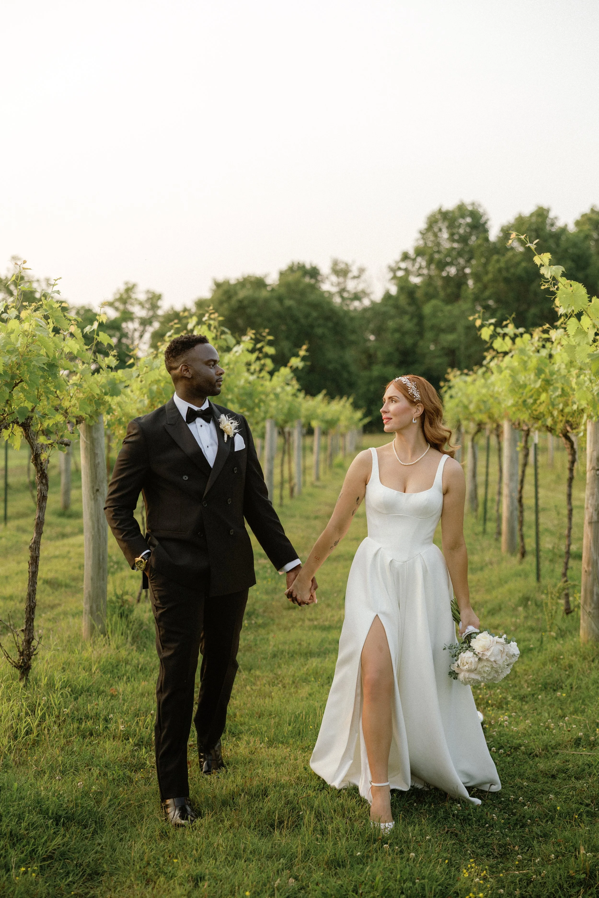 Bride and groom holding hands walking through a vineyard during their wedding day.