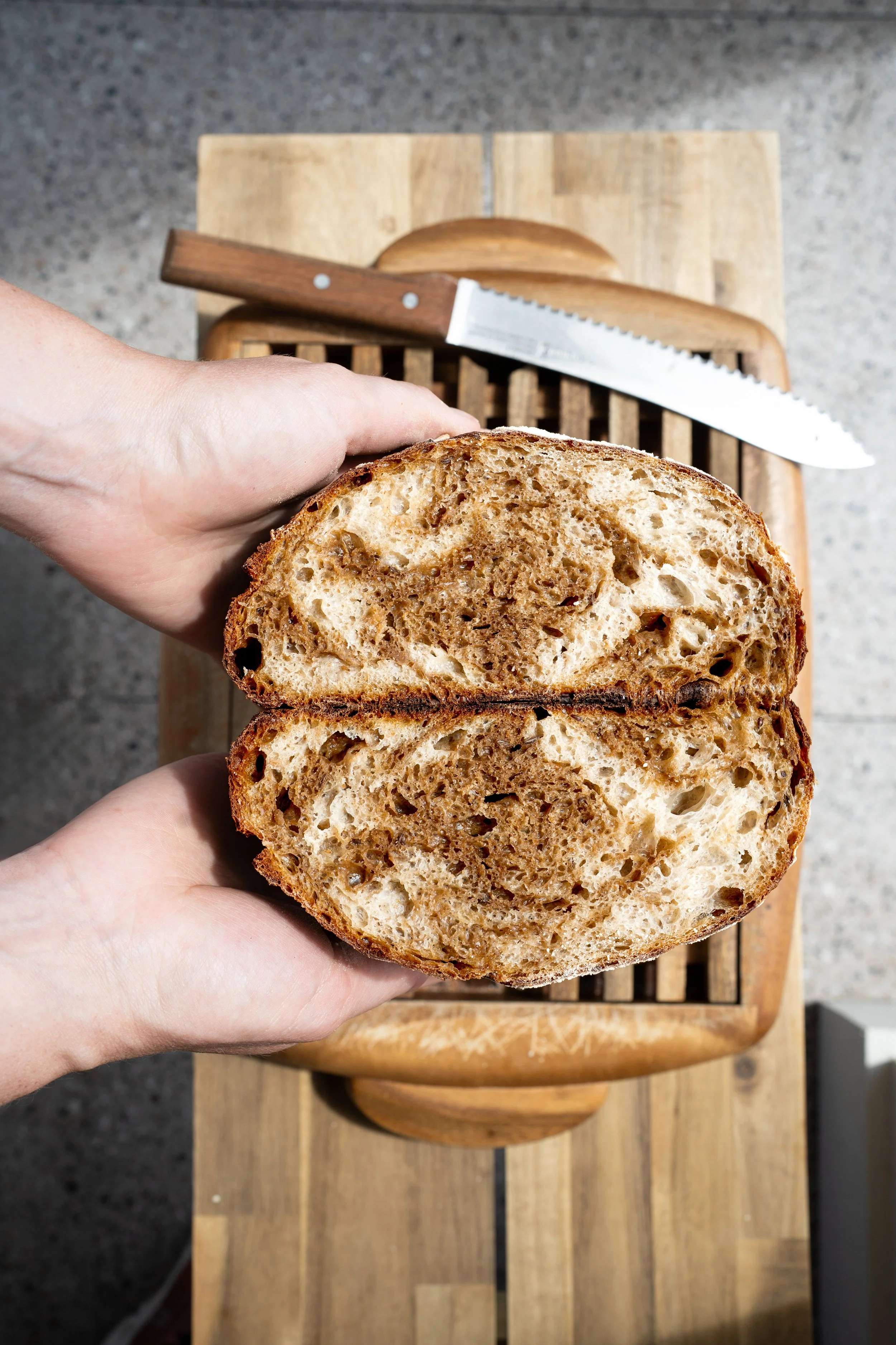 Person holding a sliced loaf of bread over a wooden cutting board with a serrated knife on top.