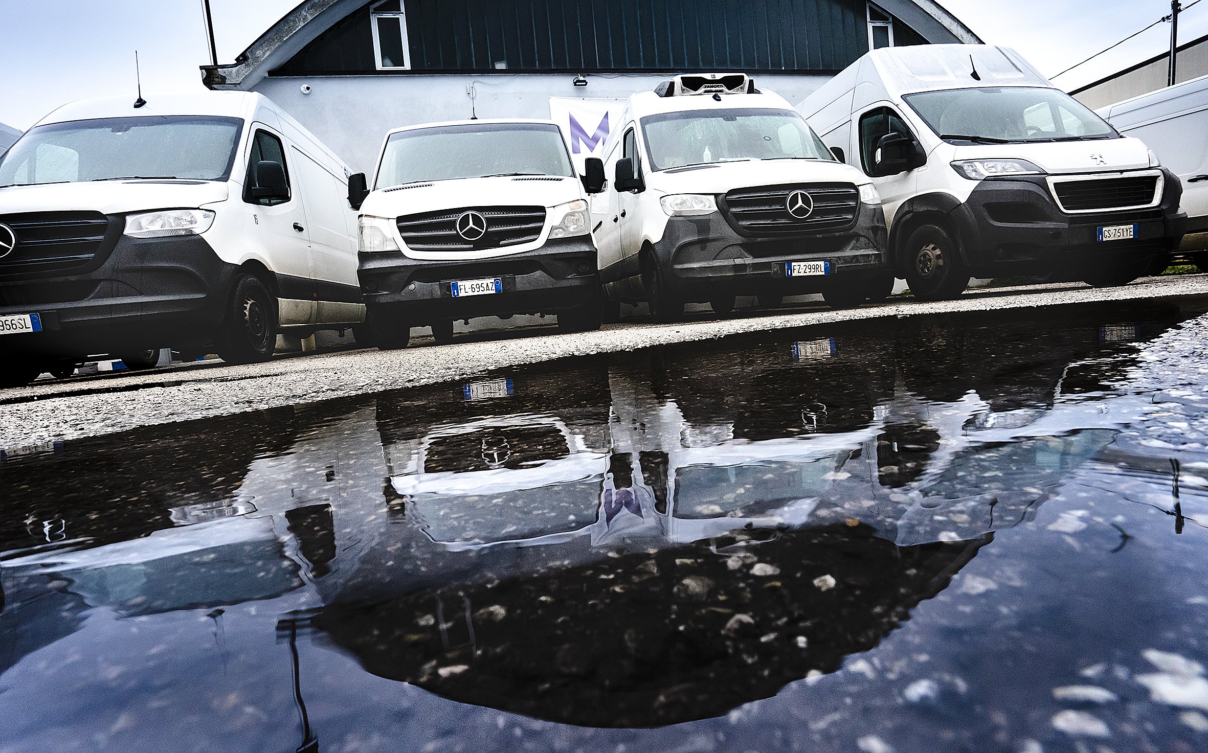 Furgoni parcheggiati di fronte a un edificio con riflesso nell'acqua.