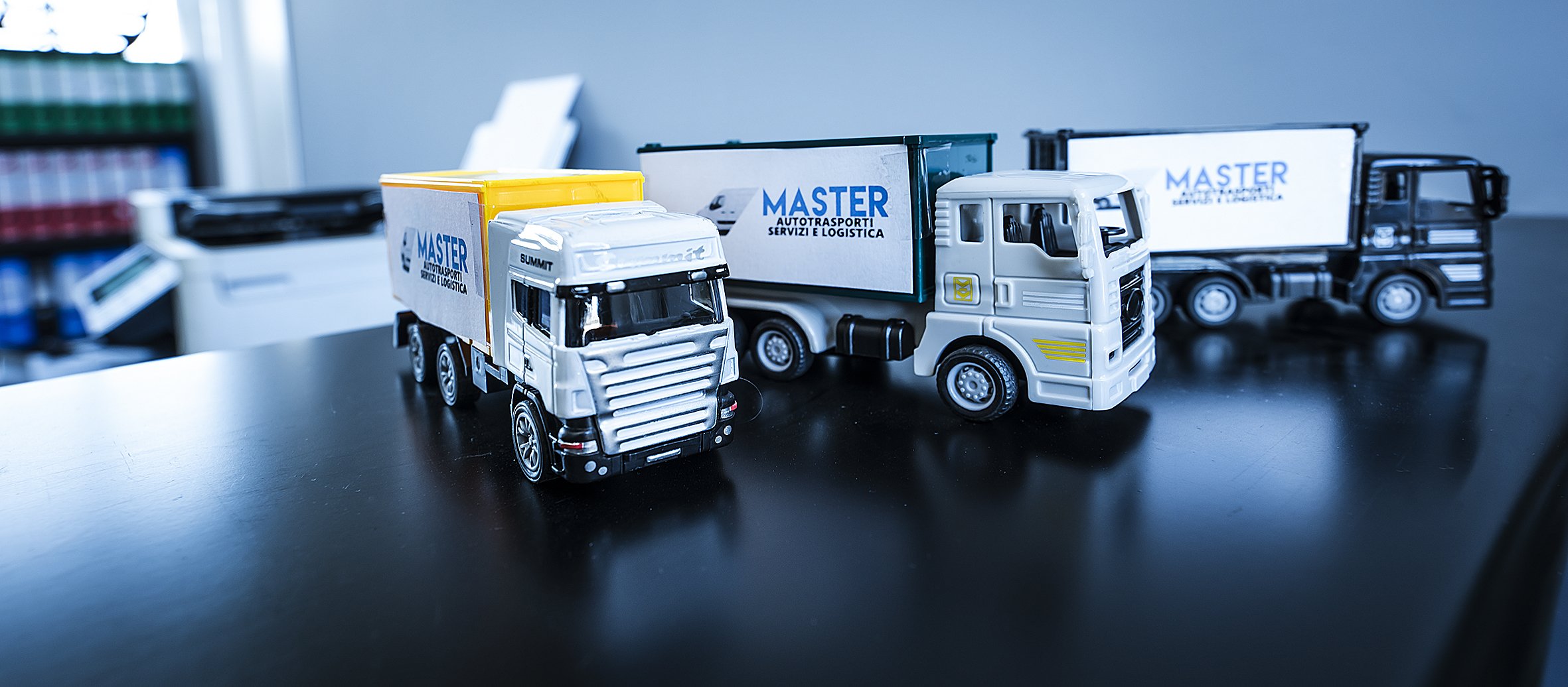 Modellini di camion su un tavolo, con il logo "Master Autotrasporti Servizi e Logistica" sui rimorchi.