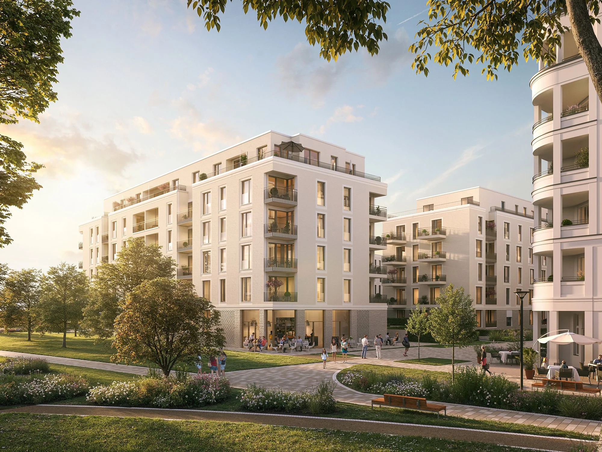 Moderne weiße Mehrfamilienhäuser mit Balkonen in einem Park mit Bäumen und Spazierwegen bei Sonnenuntergang, Menschen sitzen und spazieren