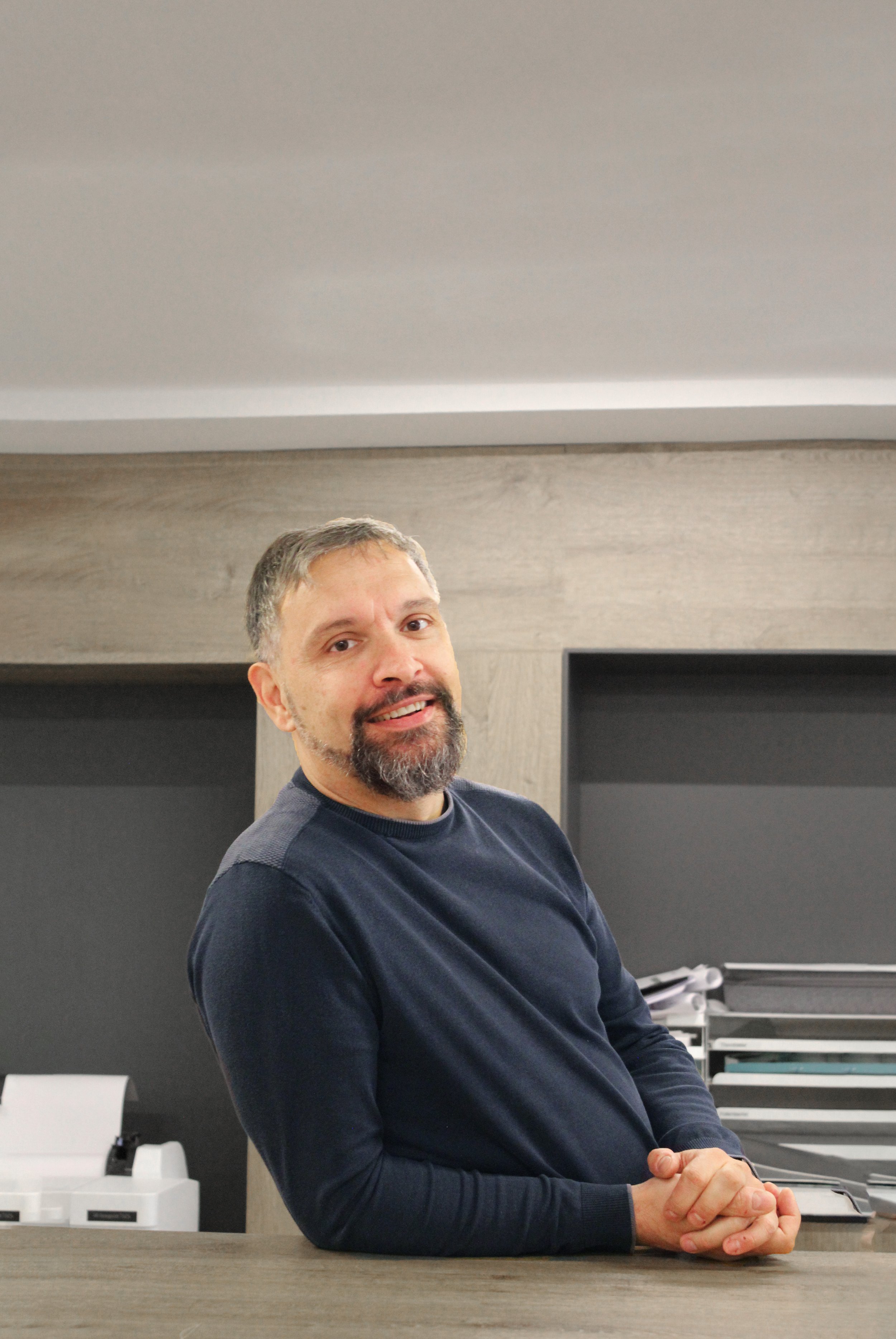 Ein Mann mit dunklem Oberteil sitzt an einem Tisch in einem modernen Raum mit Holzverkleidung an der Wand im Hintergrund.