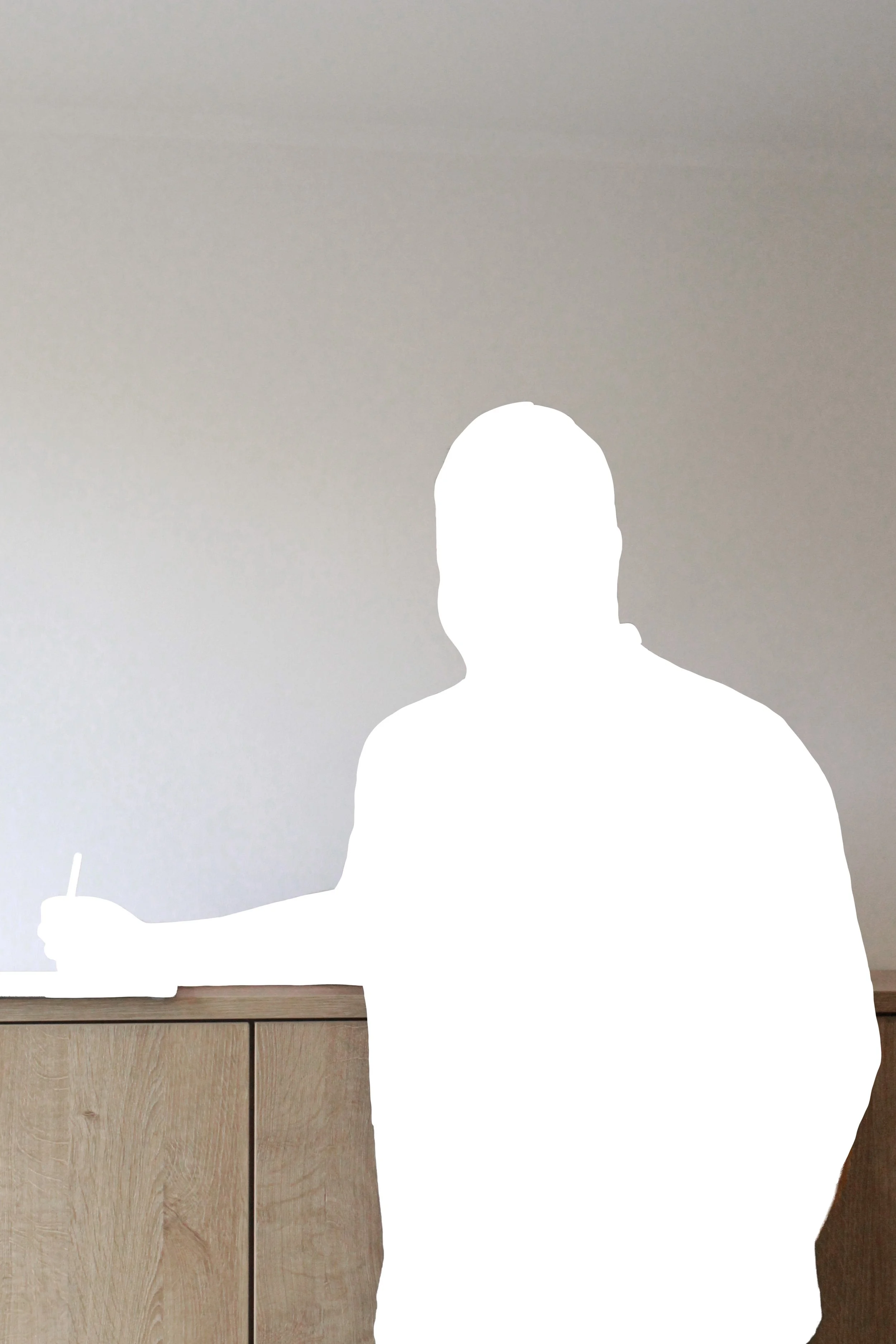 Ein silhouettierter Mensch steht an einer Holztheke, hält einen Stift in der Hand, vor einem neutralen, hellgrauen Hintergrund.