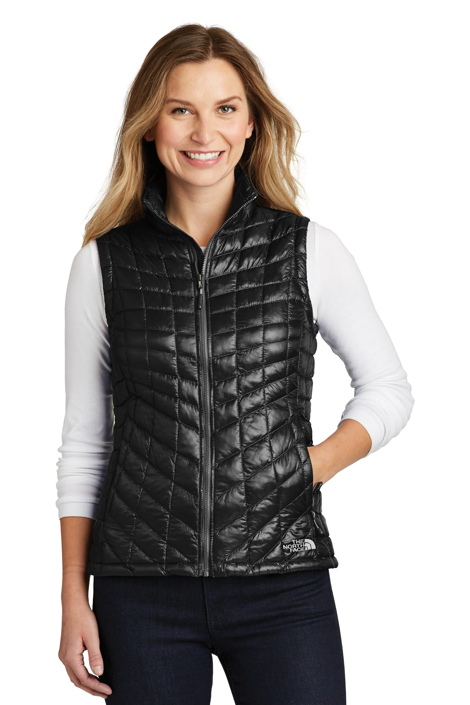 Woman smiling, wearing a black north face puffer vest over a white long-sleeve shirt, standing against a white background.