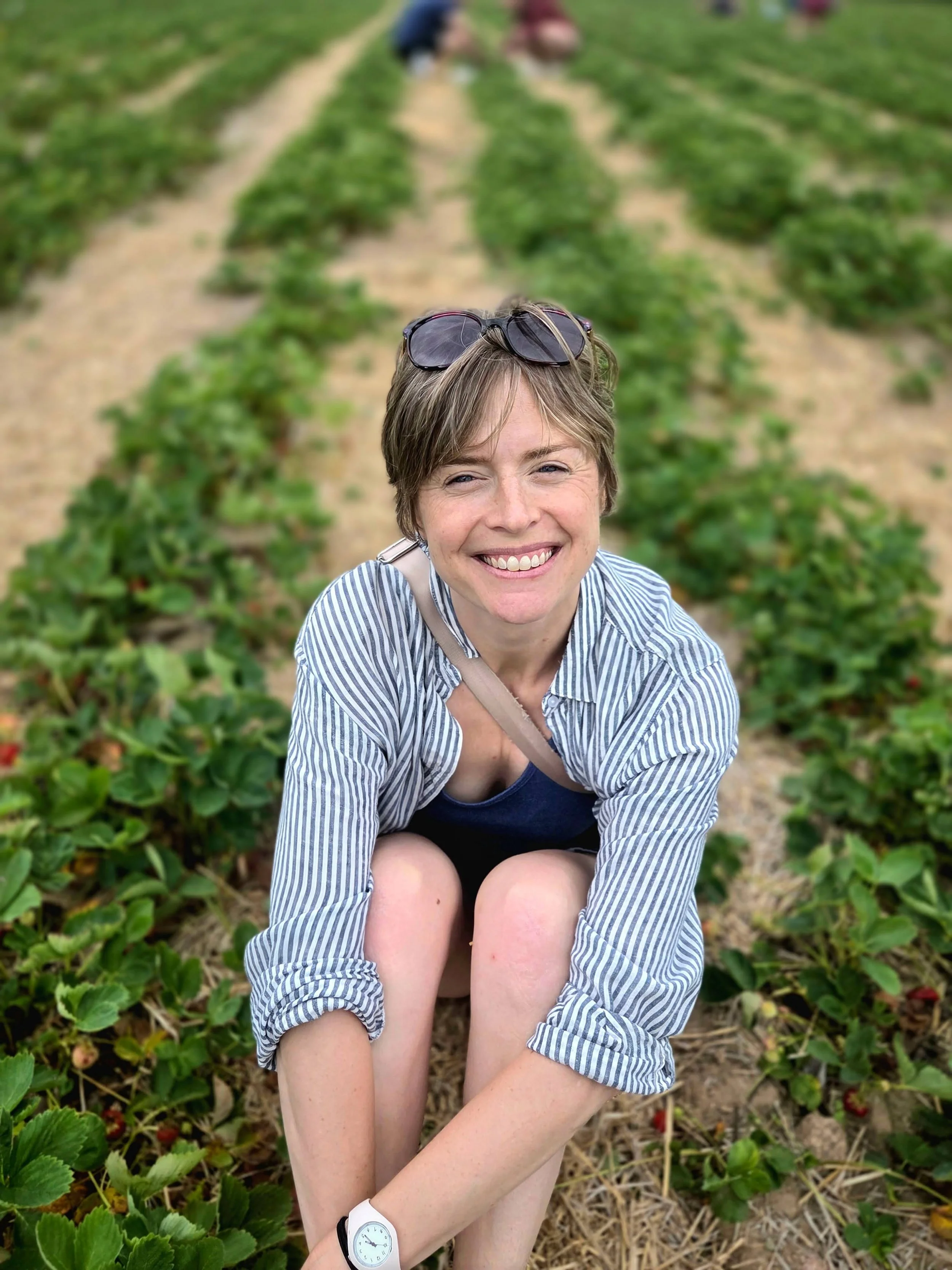 A smiling woman sitting outdoors in a strawberry field.