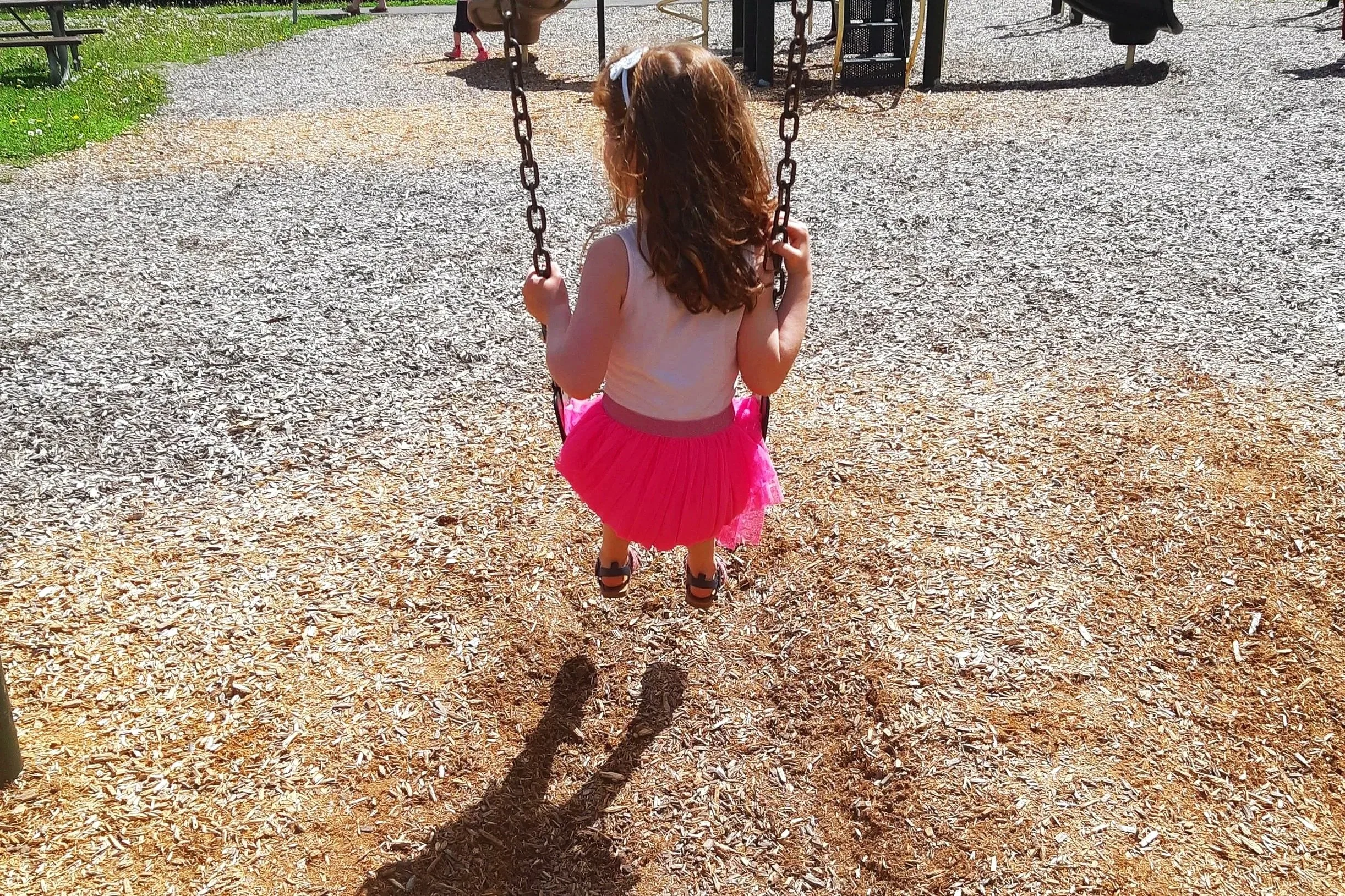 A child sitting on a swing at a playground, with her back facing the camera.