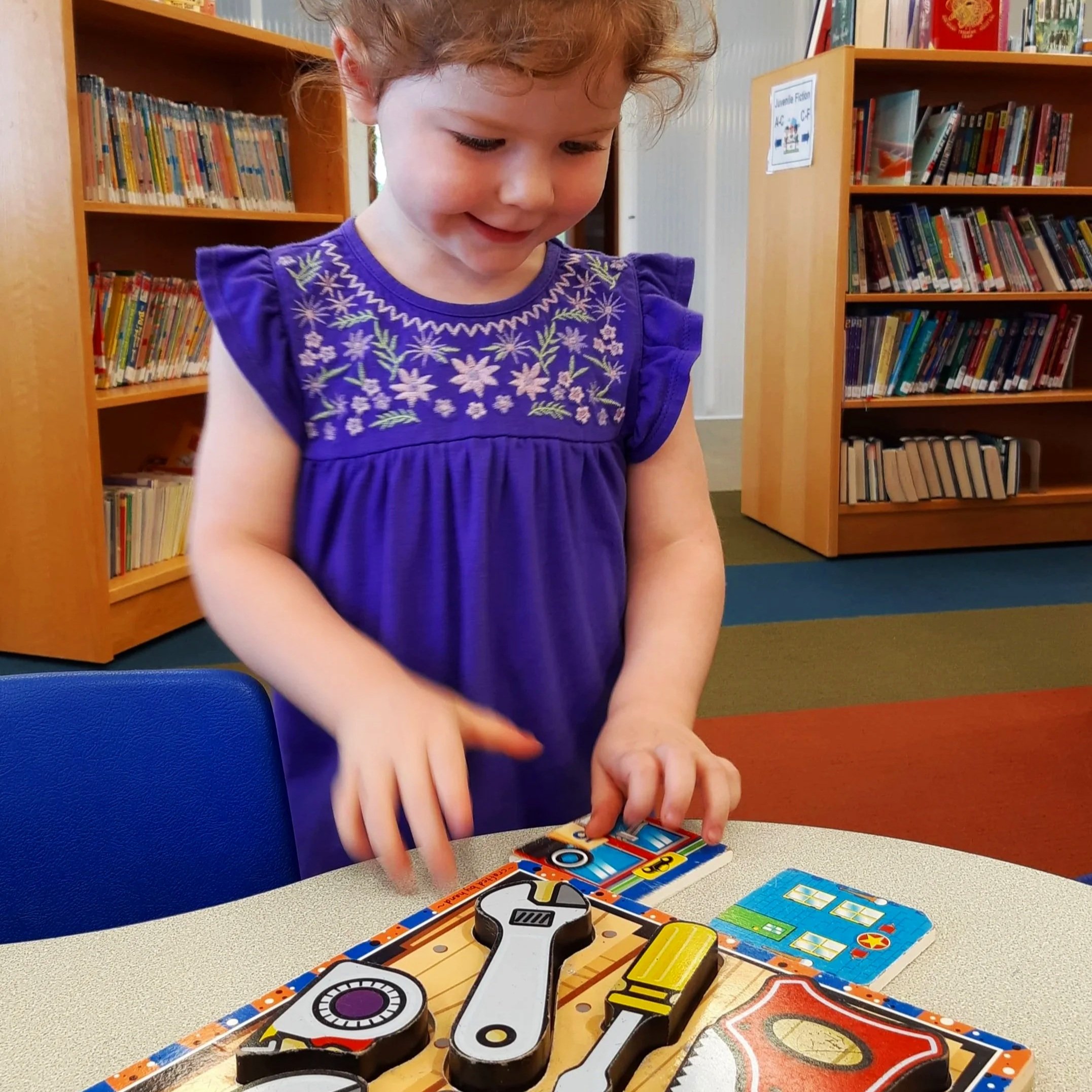 A young girl with curly hair is playing with a puzzle at a table.