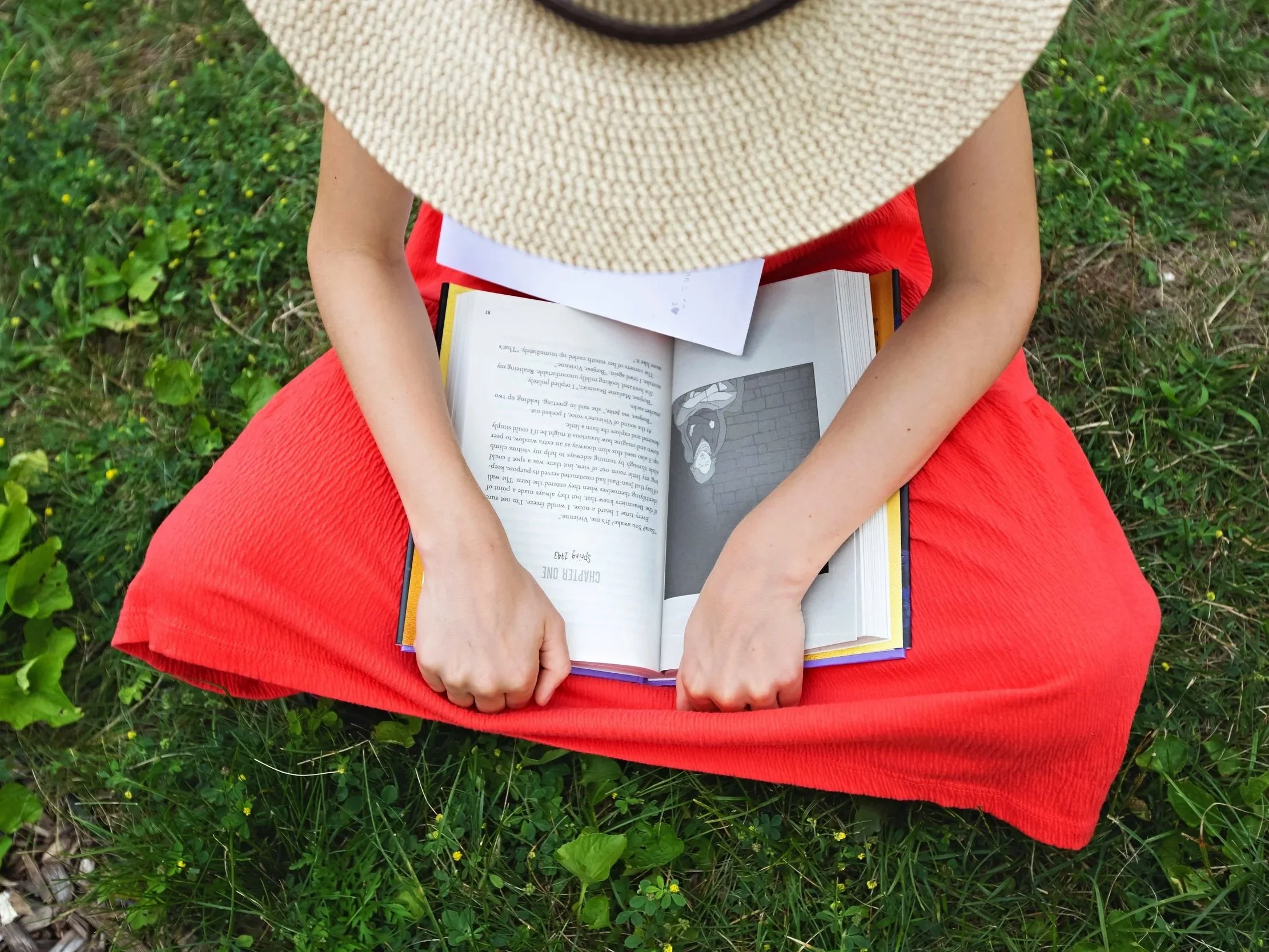 Child sitting on grass while reading a book.