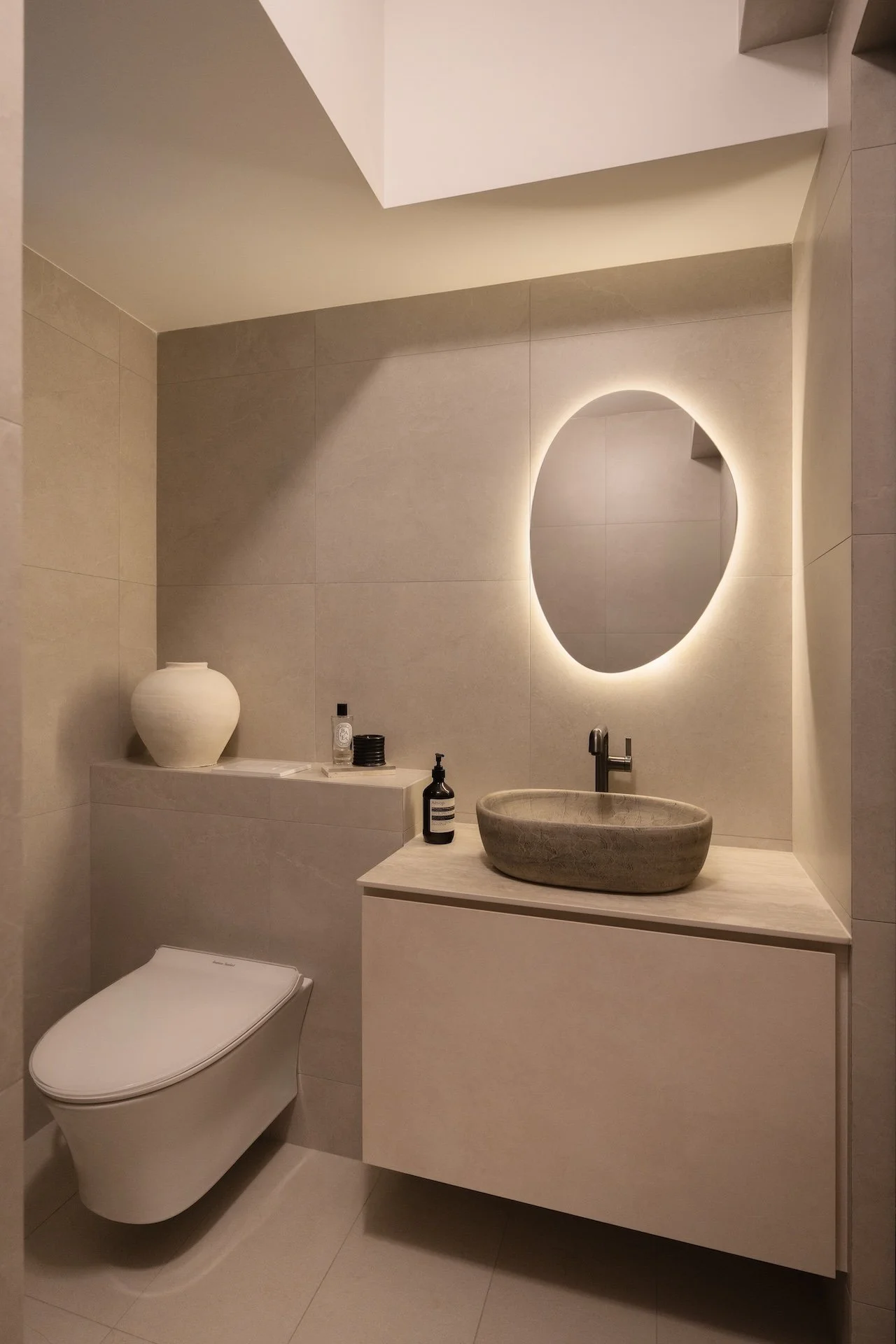 Modern bathroom with beige tiles, a round backlit mirror, a vessel sink, a floating vanity, and a concealed toilet.