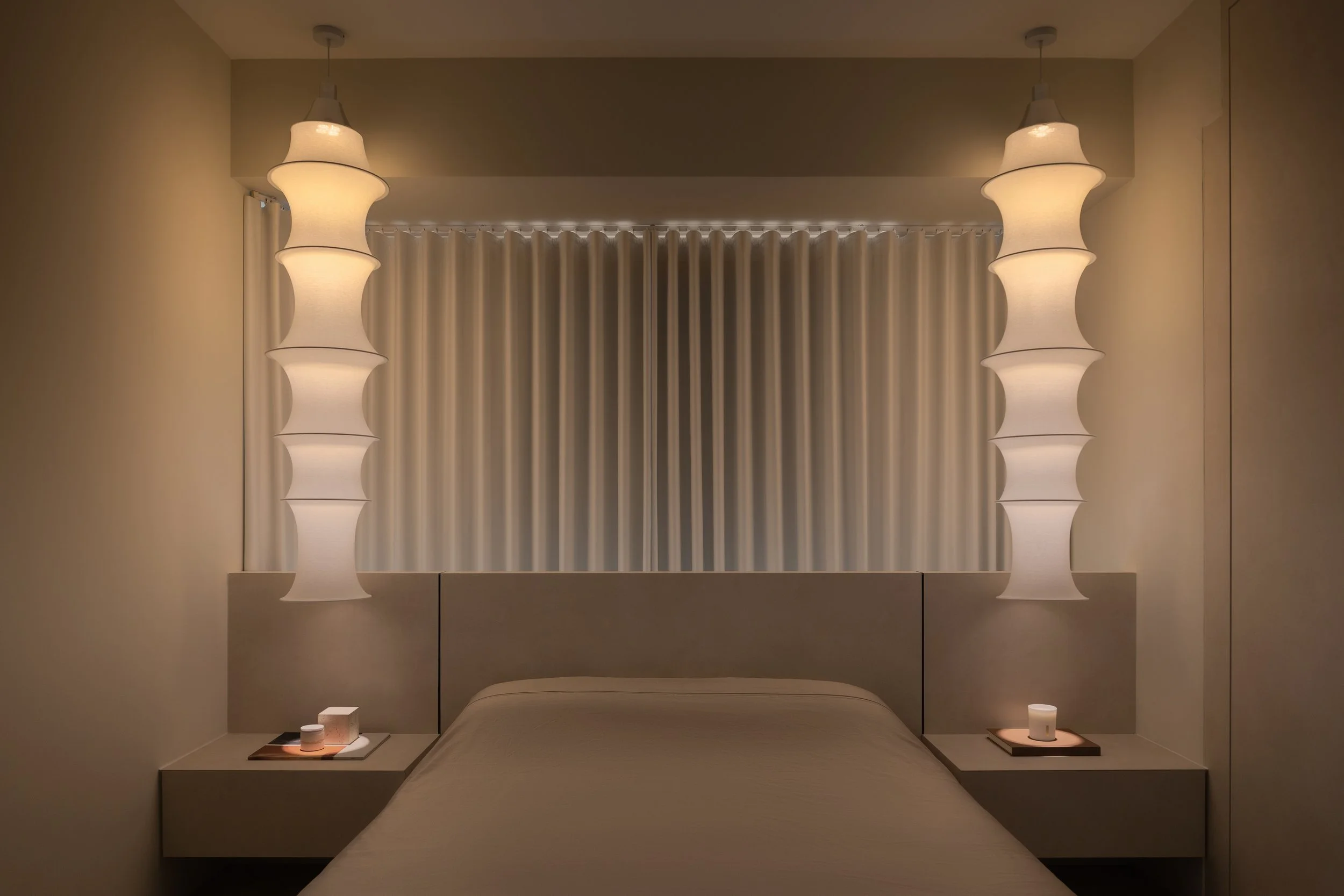 Minimalist bedroom with beige bed, two hanging pendant lamps, and nightstands with candles.