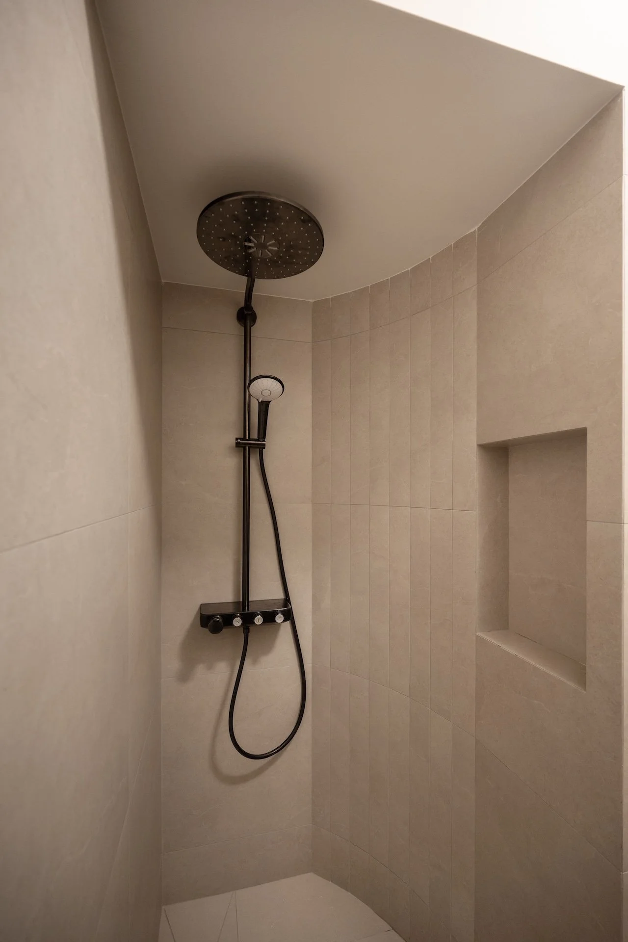 Empty shower with beige tiltile walls, a round rain shower head, and a built-in niche for toiletries.